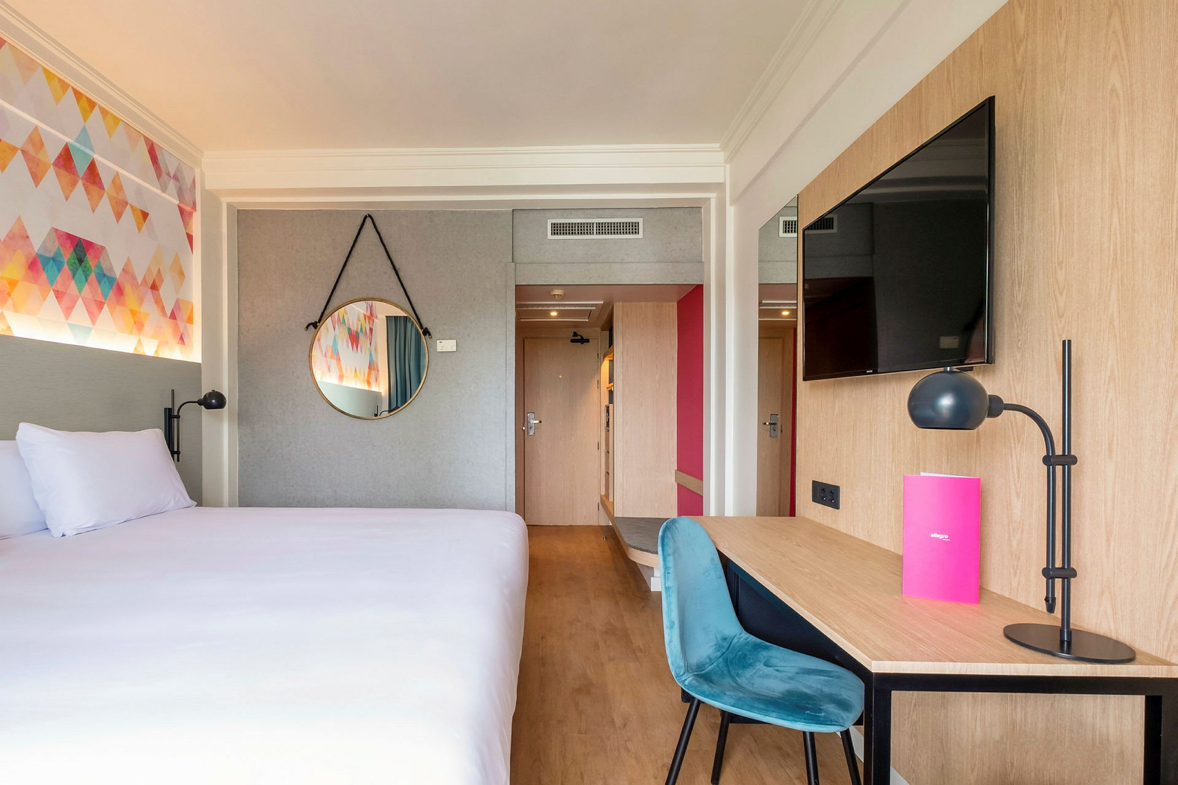Et hotelværelse med en seng, et skrivebord med stol og lampe, samt en væg-tv. (AI-genereret tekst)