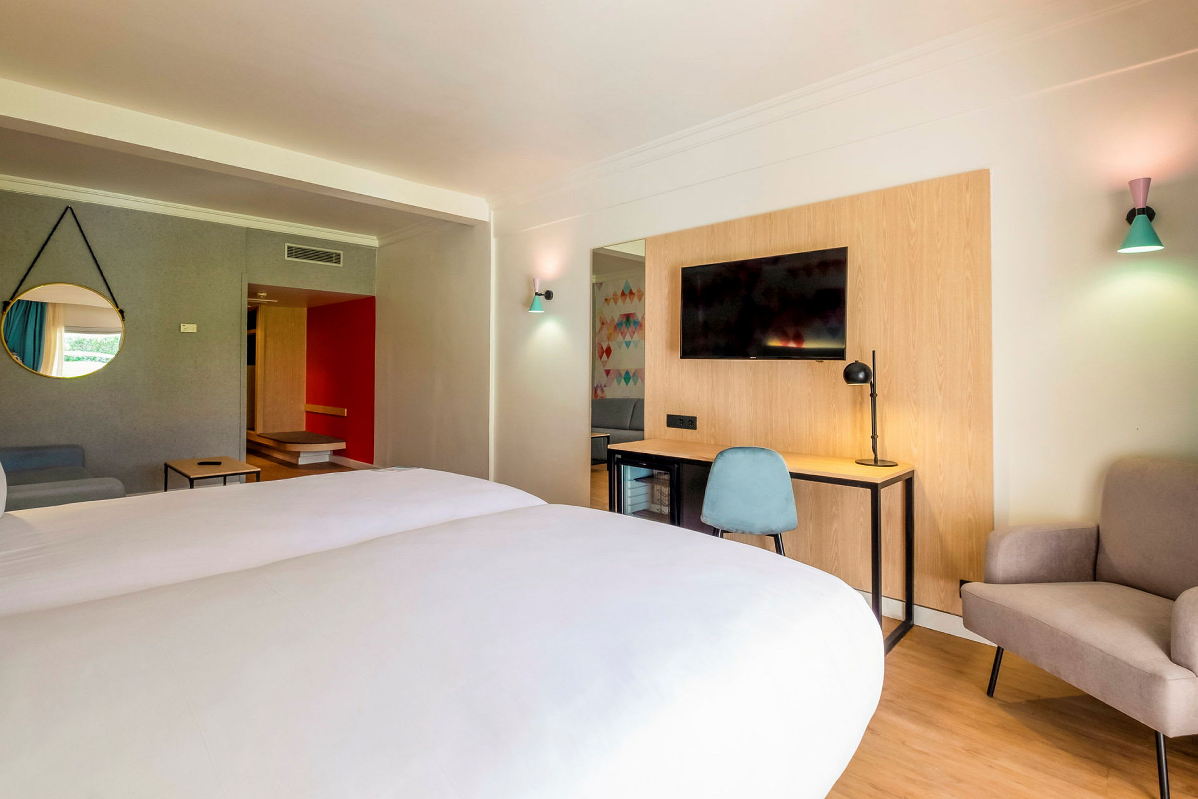 Hotelværelse med dobbeltseng, skrivebord og stol, TV samt siddeområde. (AI-genereret tekst)