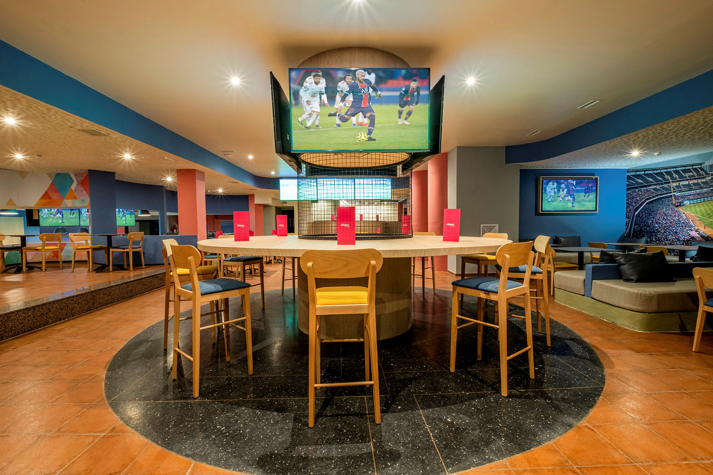 Interiør af en moderne sportsbar med siddepladser omkring et bord og flere TV-skærme. (AI-genereret tekst)
