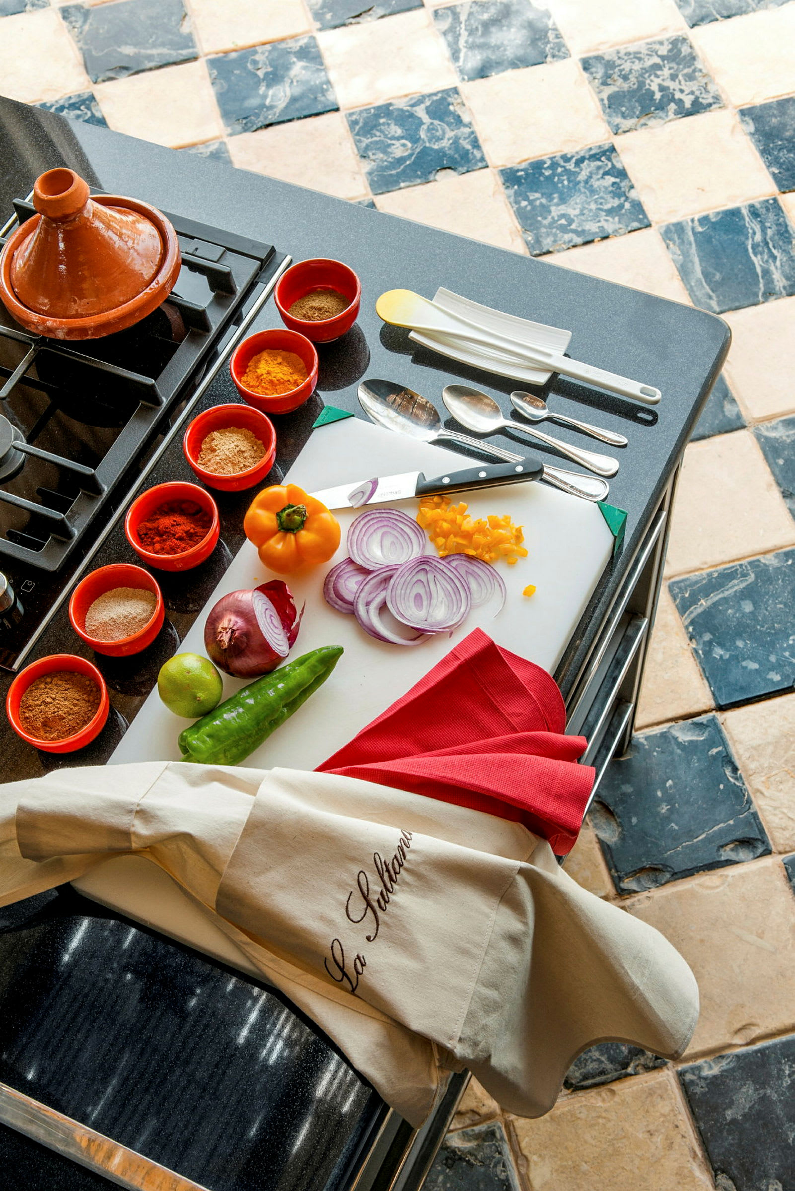 Et køkkenbord med ingredienser inklusive grøntsager, krydder og køkkenudstyr samt en taginegryde. (AI-genereret tekst)