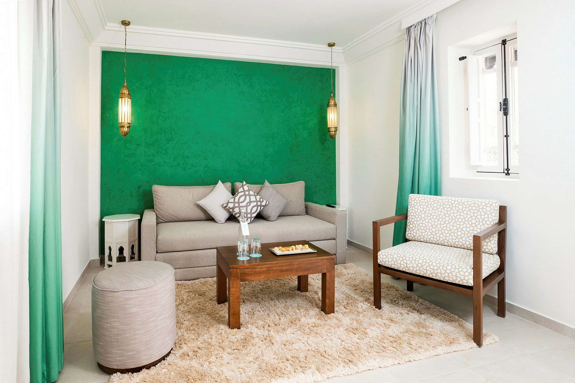 En stue med grøn væg, en beige sofa, en stol, et lille bord og et tæppe. (AI-genereret tekst)