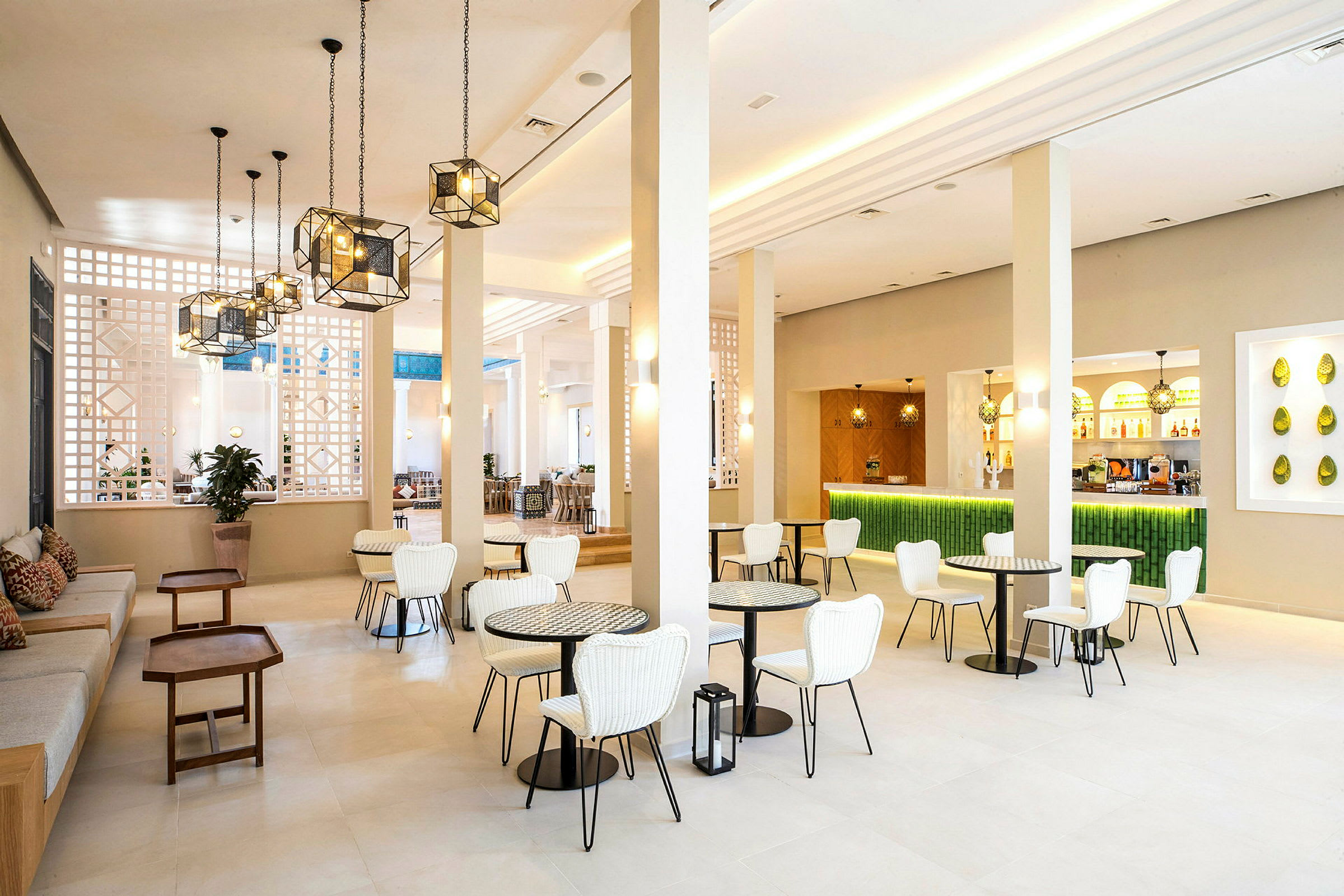 En lys og moderne lounge med hvide stole, små borde og en grøn bardisk. (AI-genereret tekst)