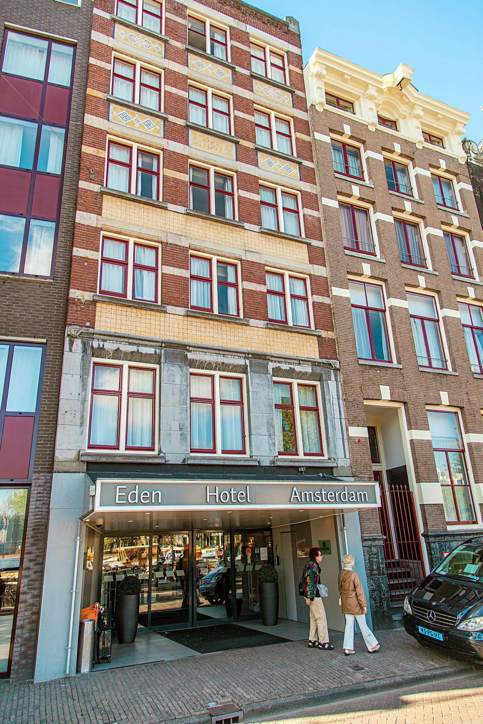 Forsiden af Eden Hotel Amsterdam med indgang og personer foran bygningen. (AI-genereret tekst)