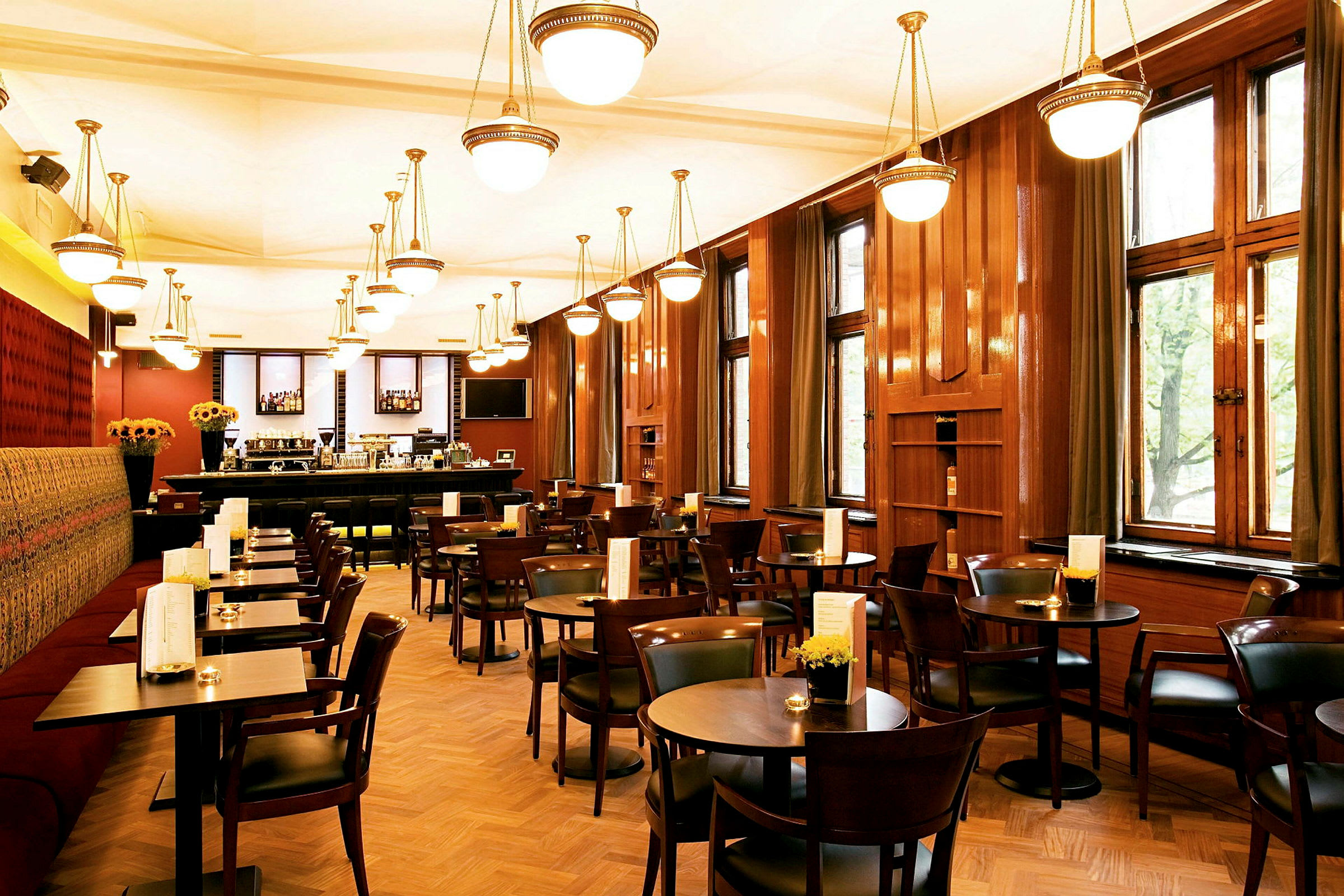 Billede af en restaurantinteriør med træborde og stole, store vinduer og hængende lamper i loftet. (AI-genereret tekst)