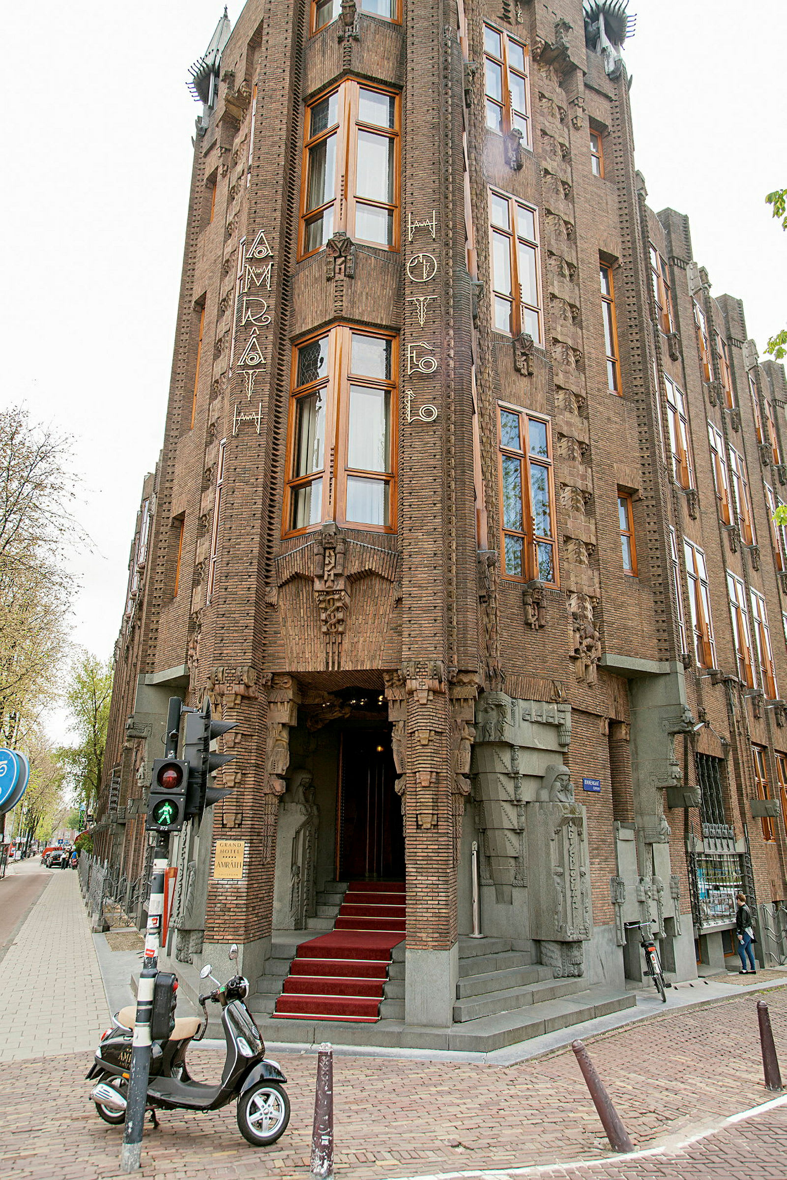 En bygning med kunstnerisk designet facade og indgang. En rød løber fører op til indgangen, og en scooter er parkeret i forgrunden. (AI-genereret tekst)