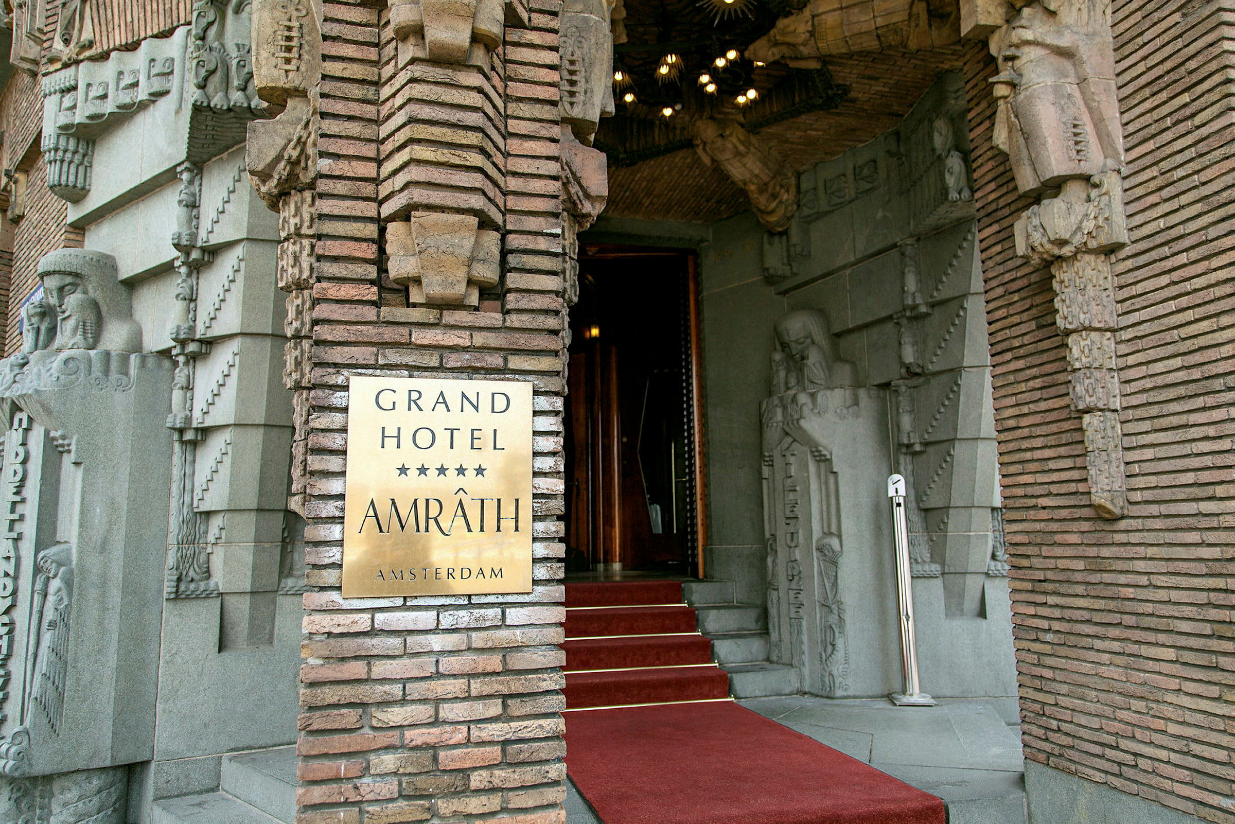 Indgangsdør til Grand Hotel Amrâth Amsterdam med dekorative stenudsmykninger. (AI-genereret tekst)