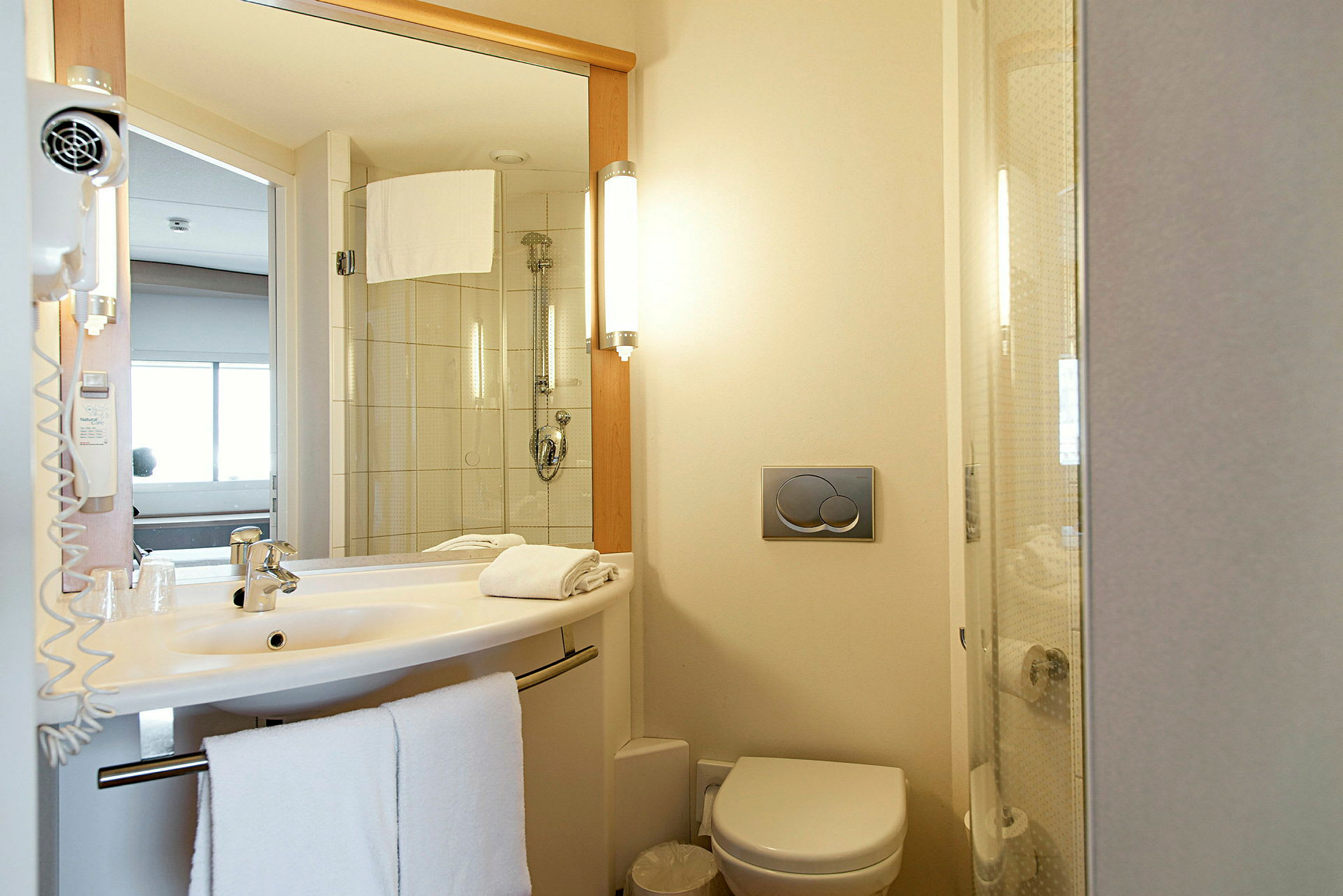 Et hotelbadeværelse med håndvask, toilet og bruser. (AI-genereret tekst)