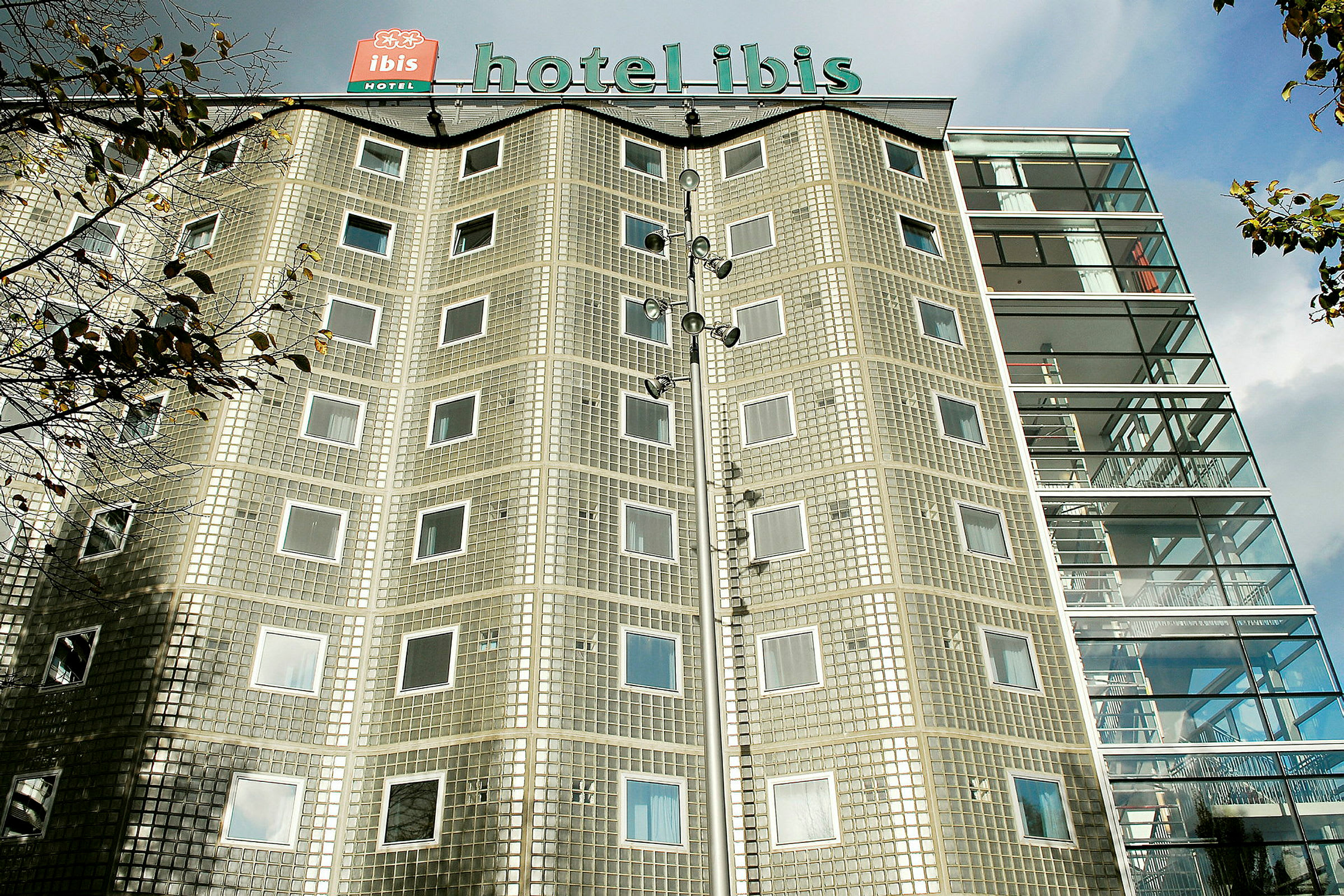 Bygning med hotellets navn på taget og facade af glasblokke samt vinduer. (AI-genereret tekst)
