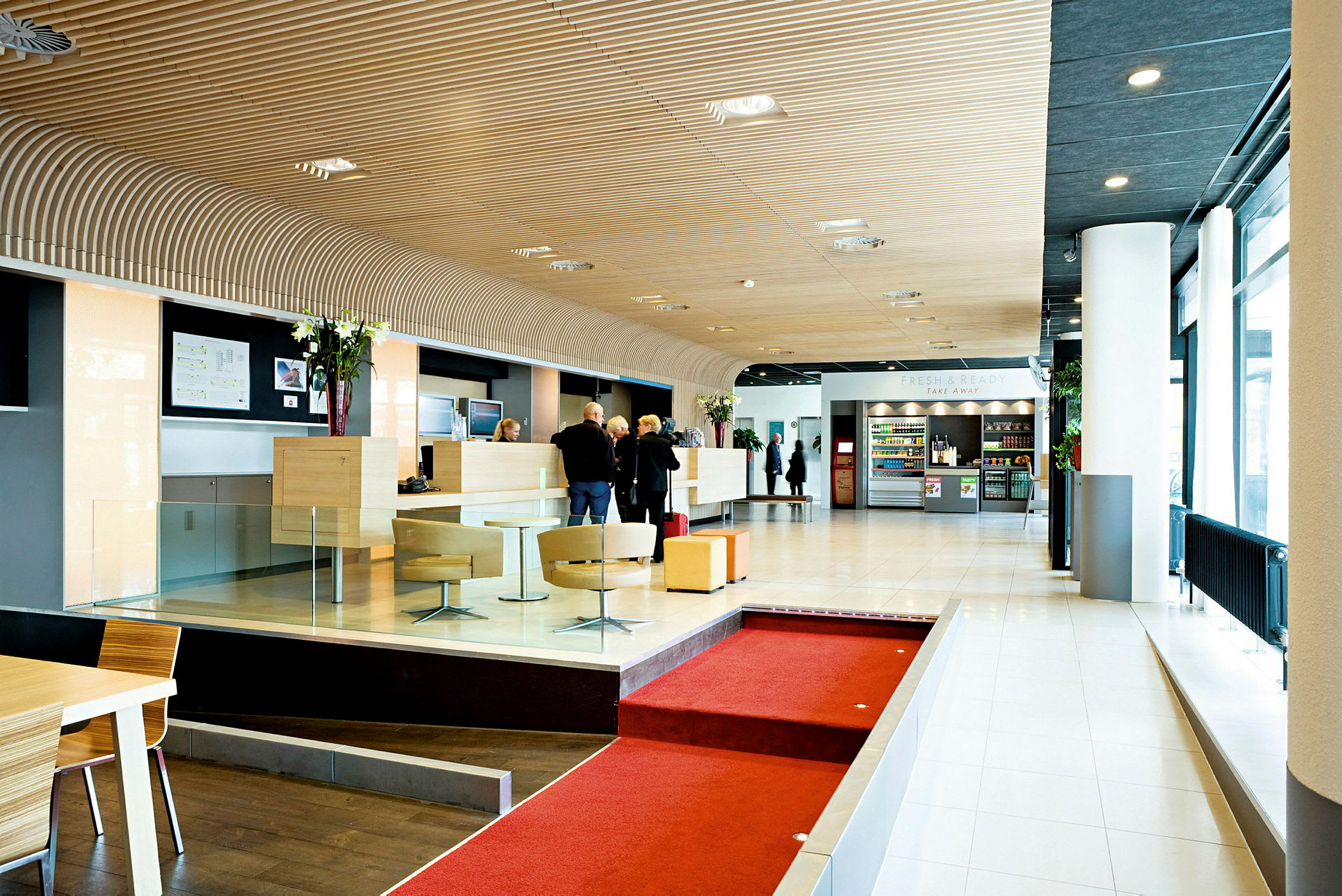 Lys og moderne hotellobby med reception, siddeområder og en kiosk med drikkevarer og snacks. (AI-genereret tekst)