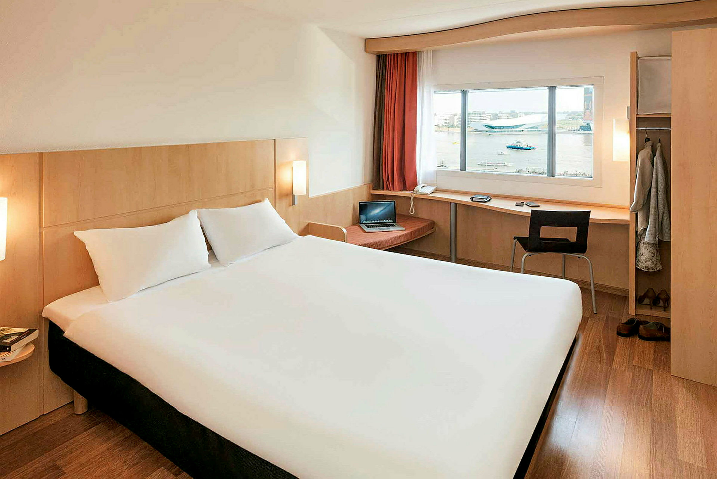 Et hotelværelse med en stor seng, skrivebord ved vinduet og garderobe. (AI-genereret tekst)