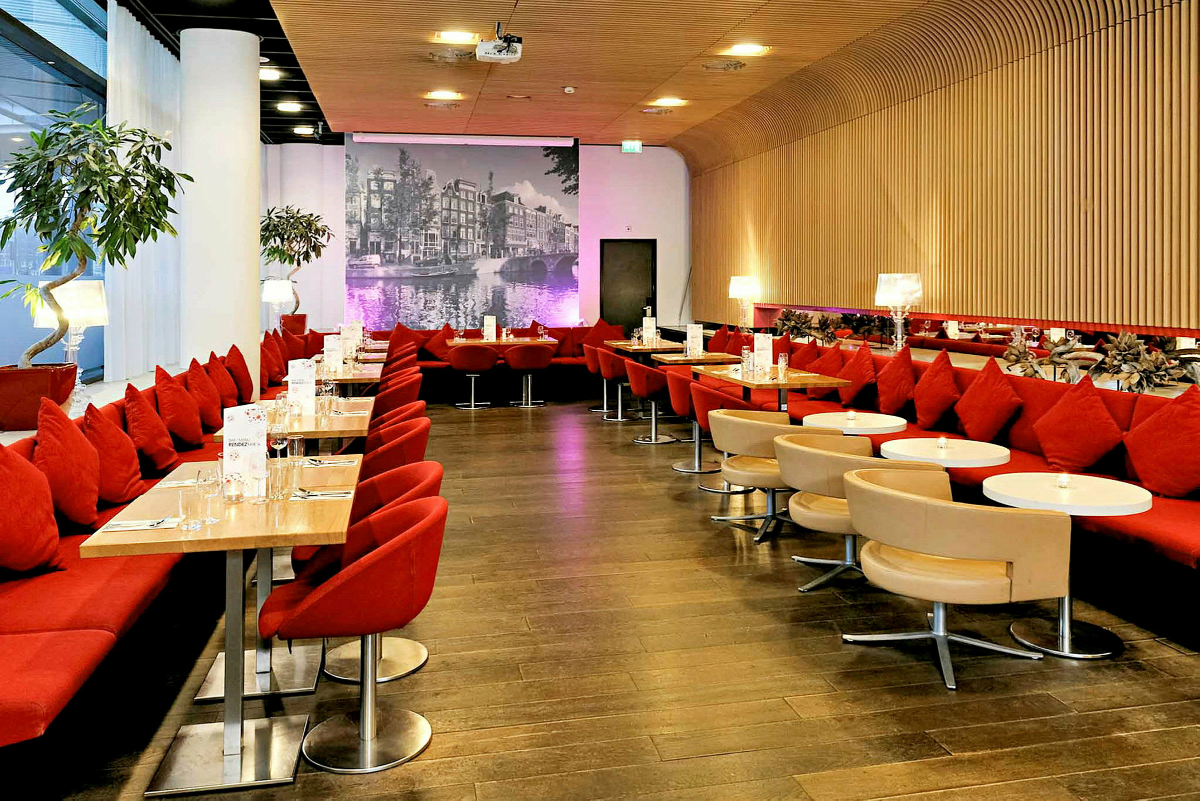 Stemningsfuld restaurant med røde siddepladser, små borde og en baggrundsvæg med et sort-hvidt bybillede. (AI-genereret tekst)