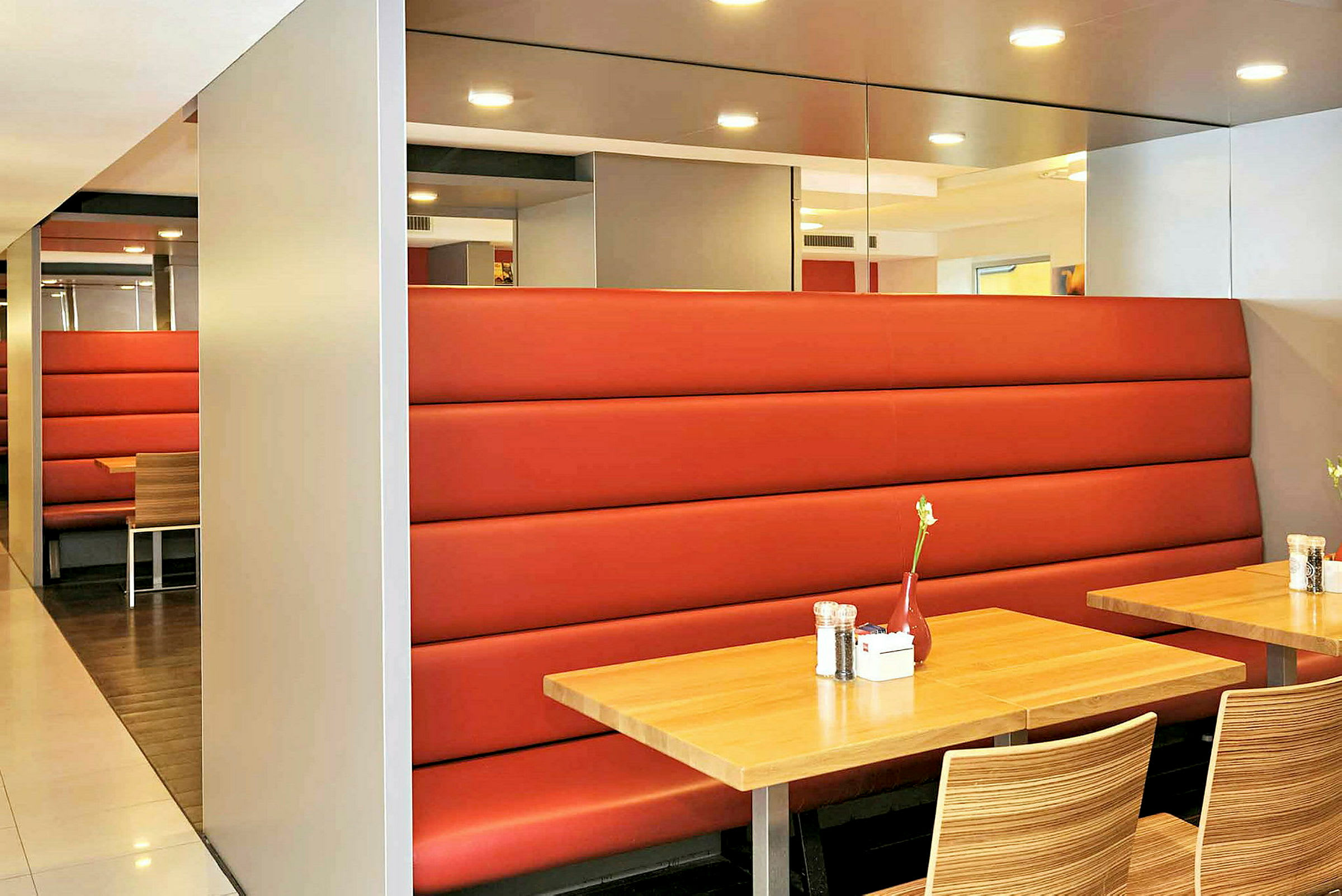 En indretning af en restaurant med træborde, røde sofaer og stole med træmønster. (AI-genereret tekst)