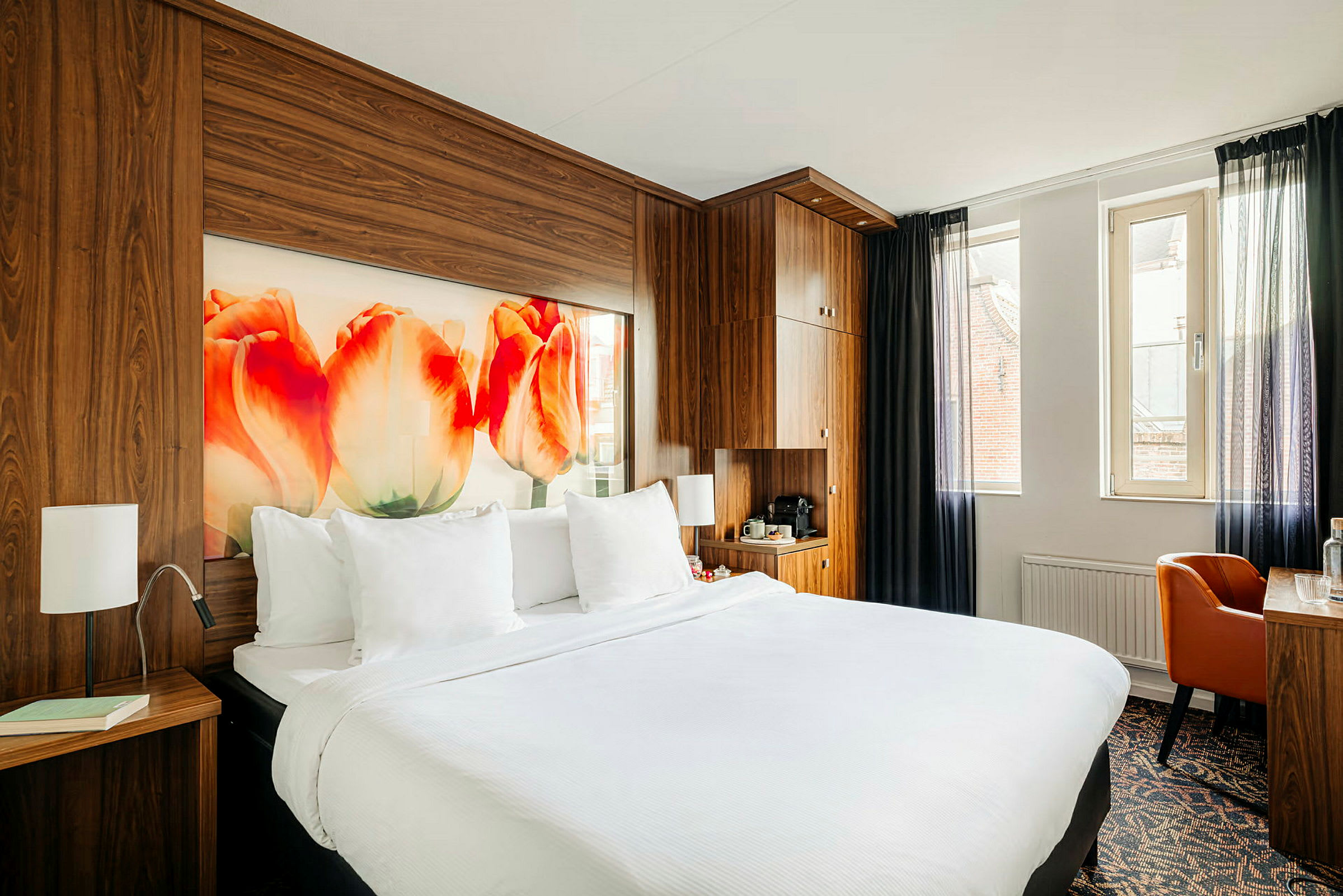 Hotelværelse med en dobbeltseng, træpaneler, tulipanmotiv på væggen og et skrivebord ved vinduet. (AI-genereret tekst)