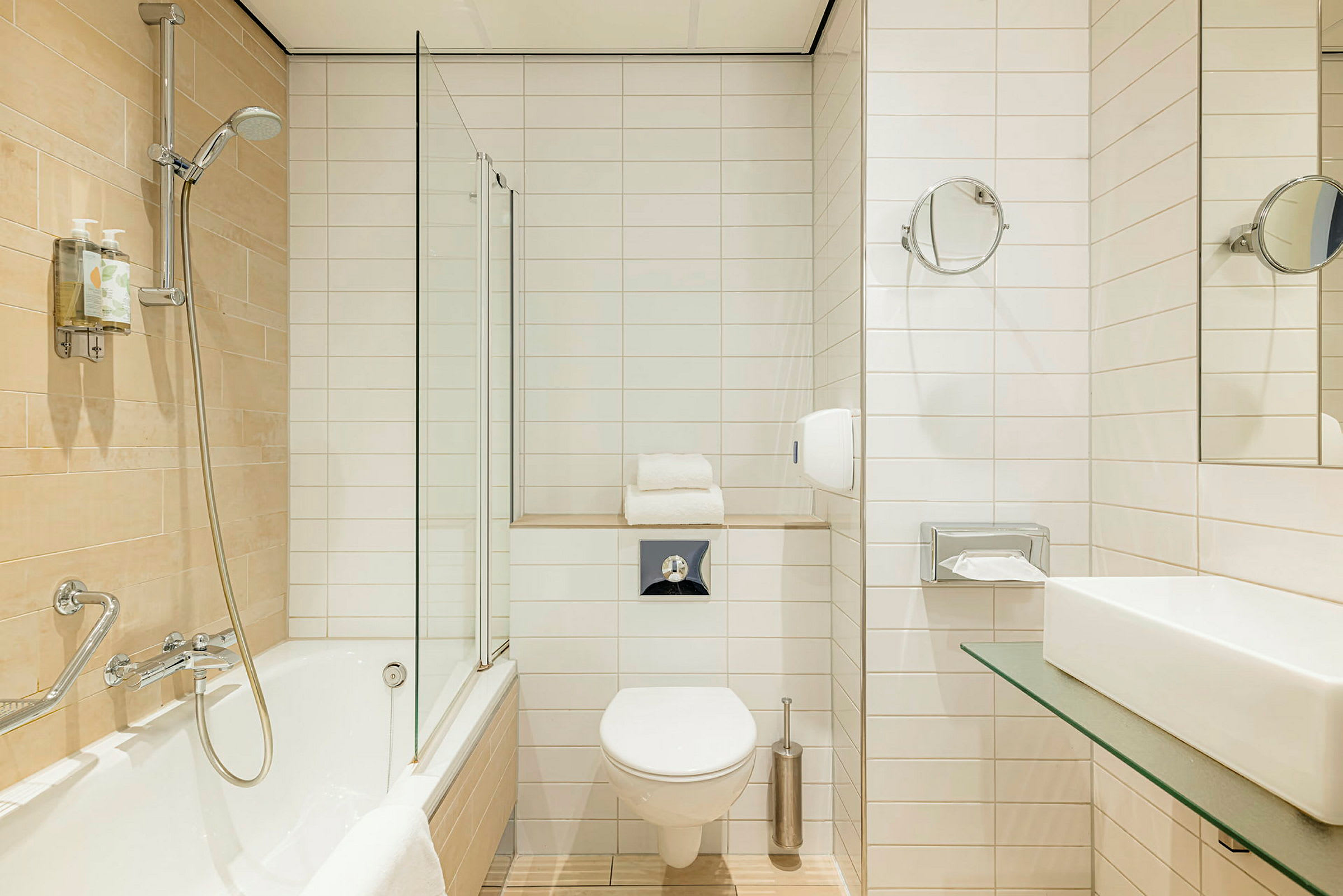 Et badeværelse med badekar og vægmonteret bruser, toilet og håndvask. (AI-genereret tekst)
