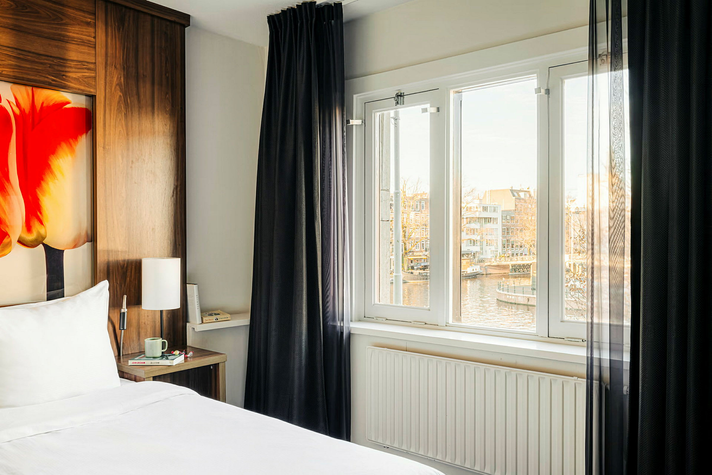 Et hotelværelse med en seng, et vindue med udsigt over en kanal og huse. (AI-genereret tekst)