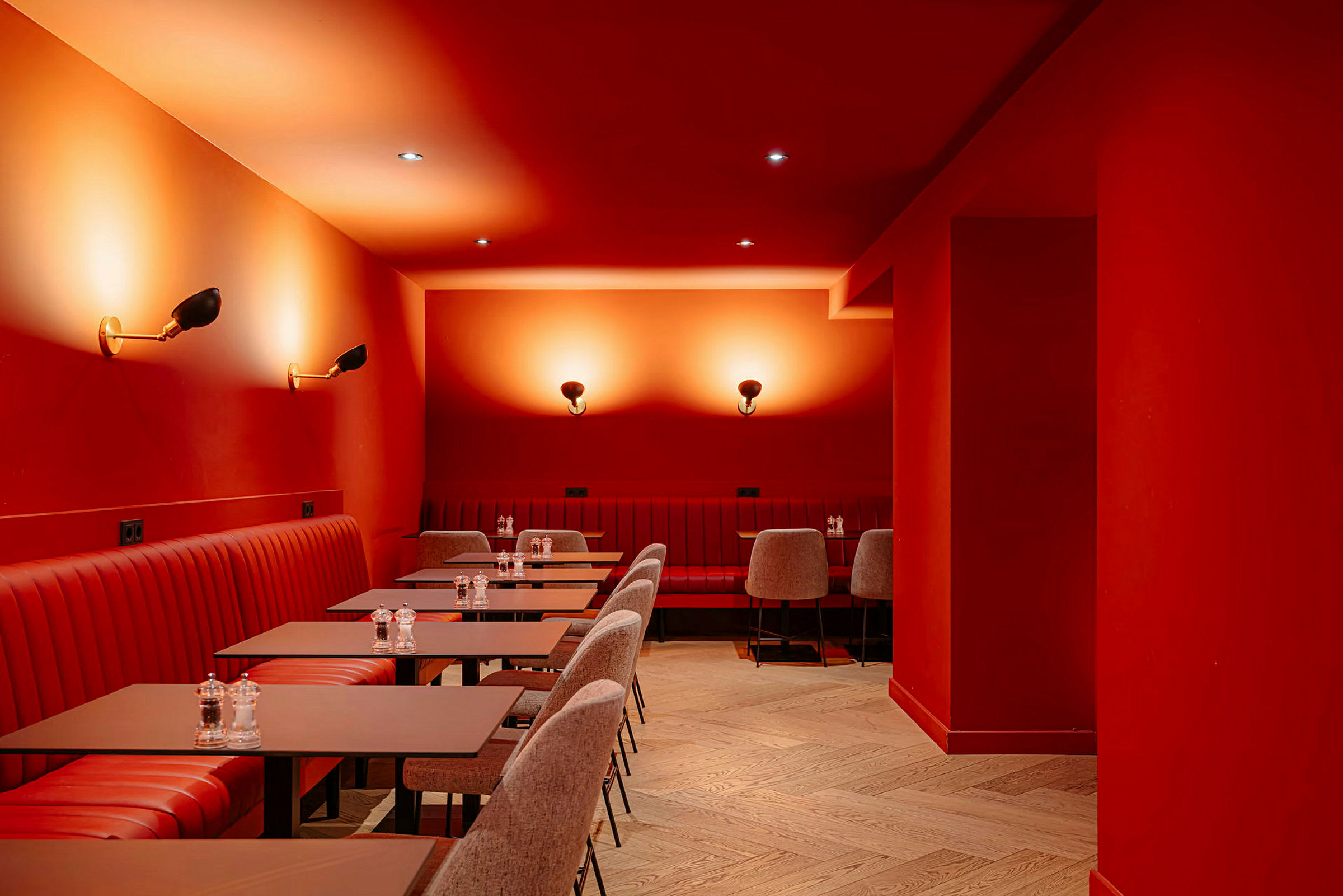 Billede af interiøret i en restaurant eller café med røde vægge og loft. Rød polstring på siddepladserne og matchende borde. Belysning med væglamper skaber en varm atmosfære. (AI-genereret tekst)