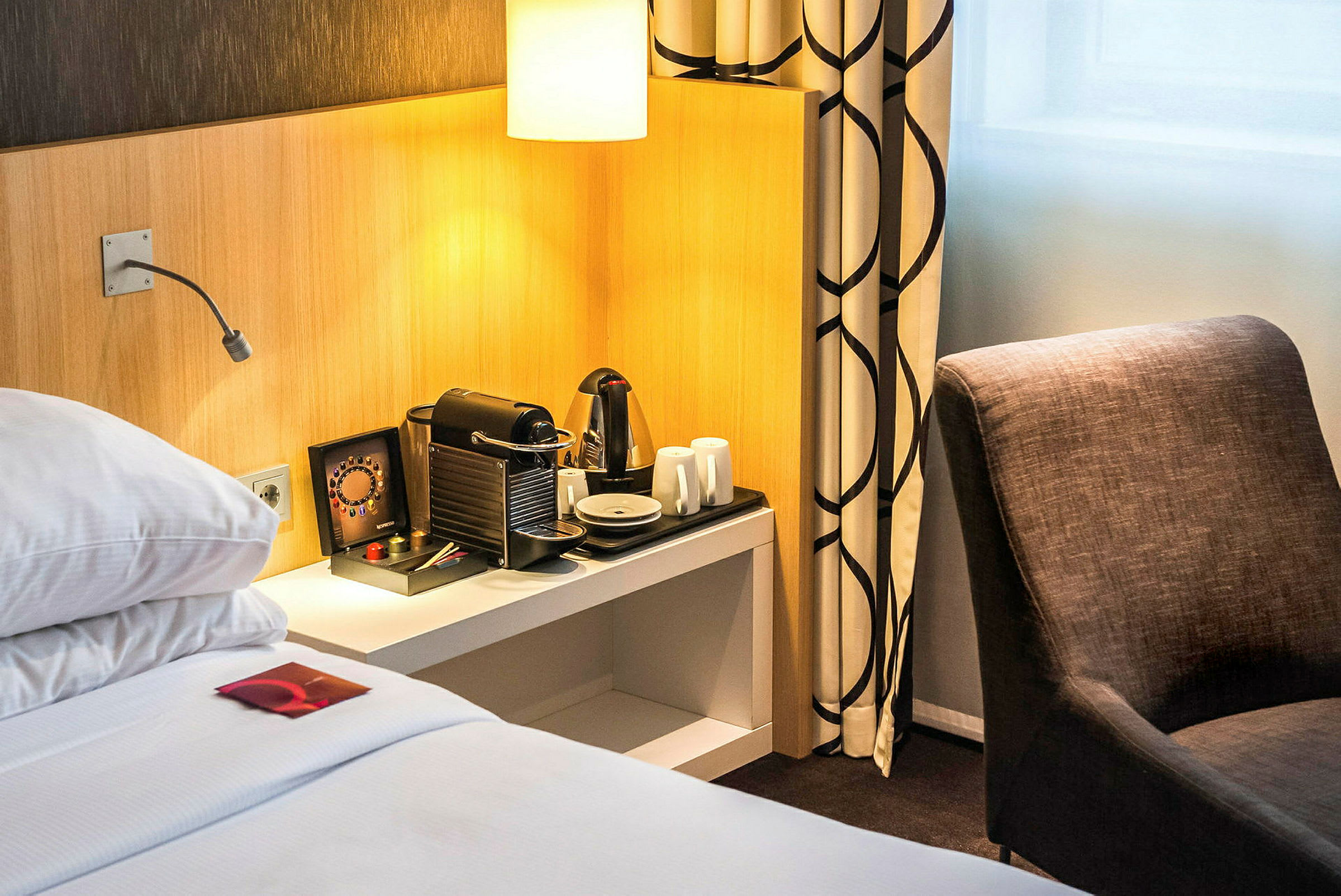 Hotelværelse med seng, kaffemaskine og stol. (AI-genereret tekst)