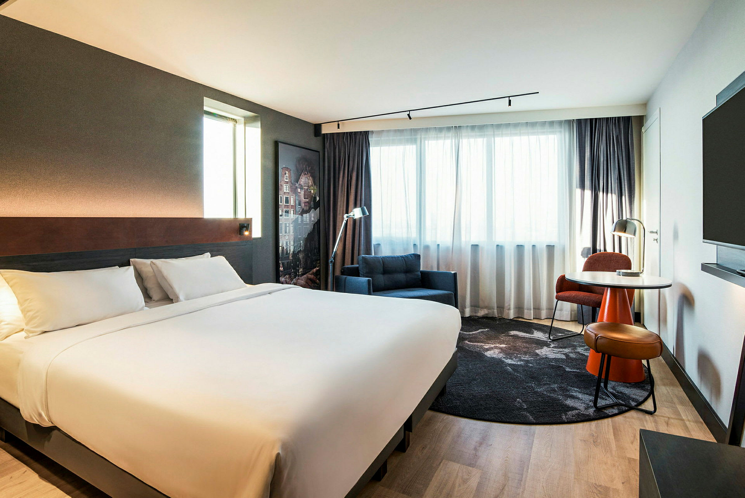 Et moderne hotelværelse med en stor dobbeltseng, lænestol og et skrivebord ved vinduet. (AI-genereret tekst)