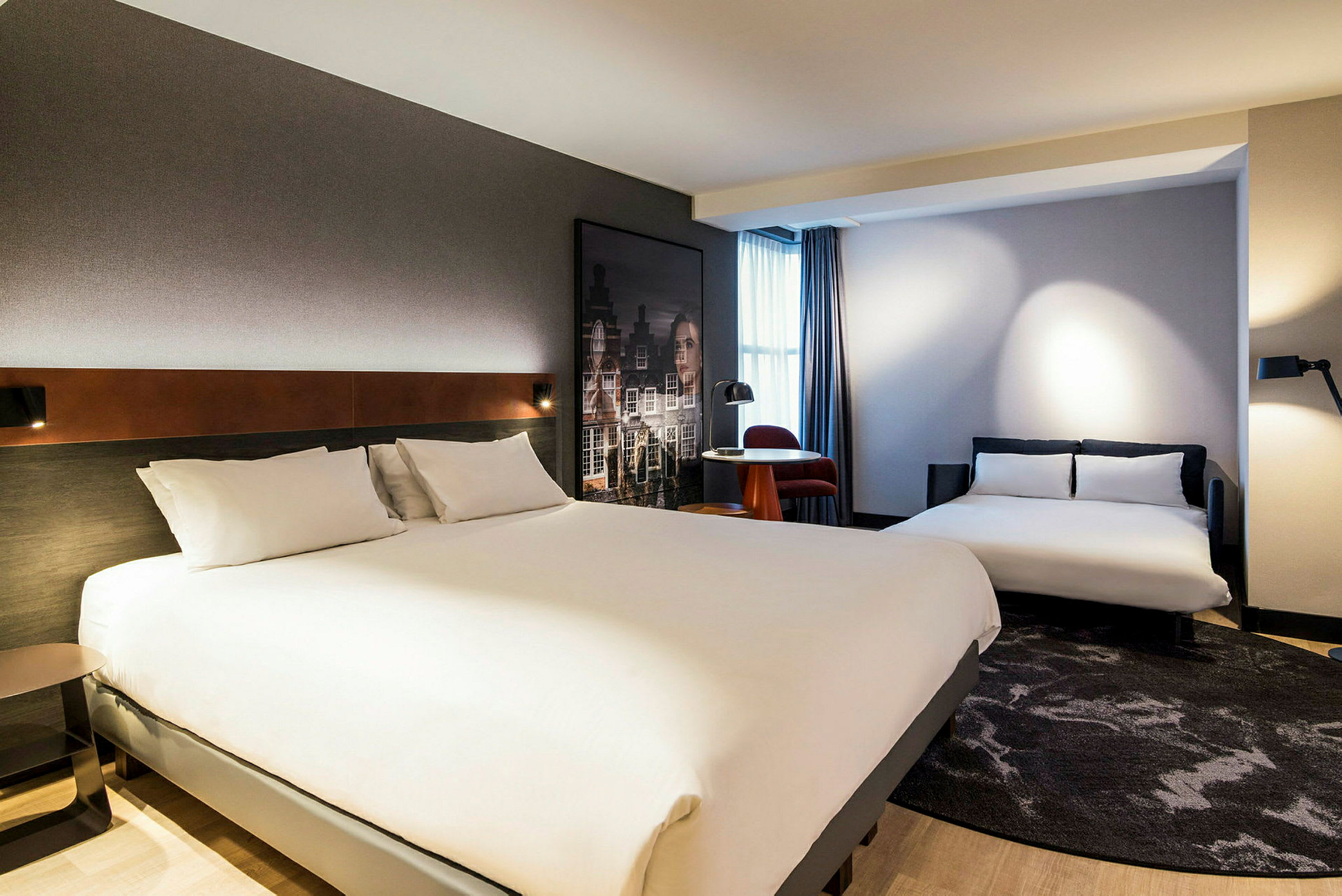 Hotelværelse med to senge og et mindre bord med en stol ved et vindue. (AI-genereret tekst)