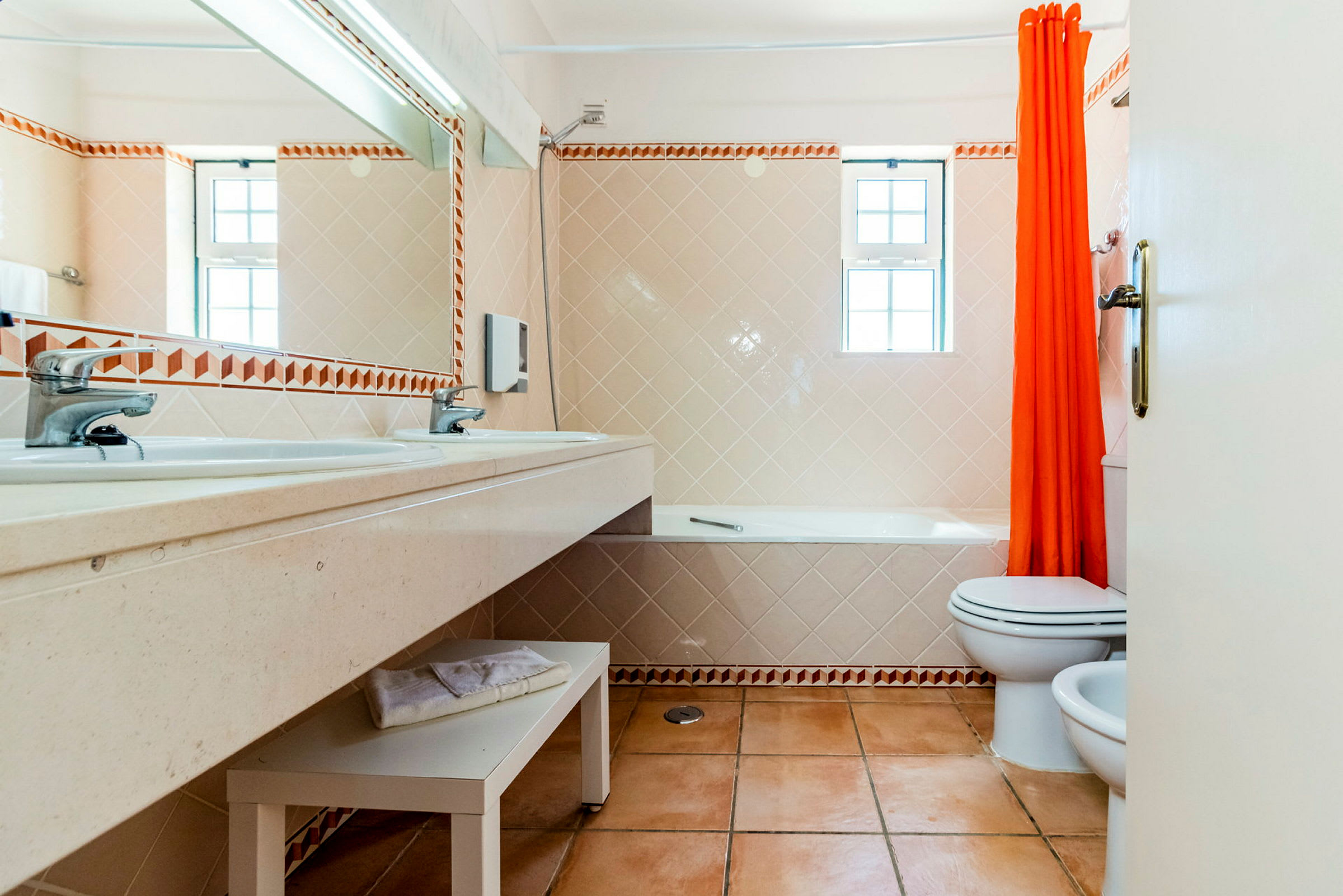 Badeværelse med håndvask, toilet og badekar med orange bruseforhæng. (AI-genereret tekst)