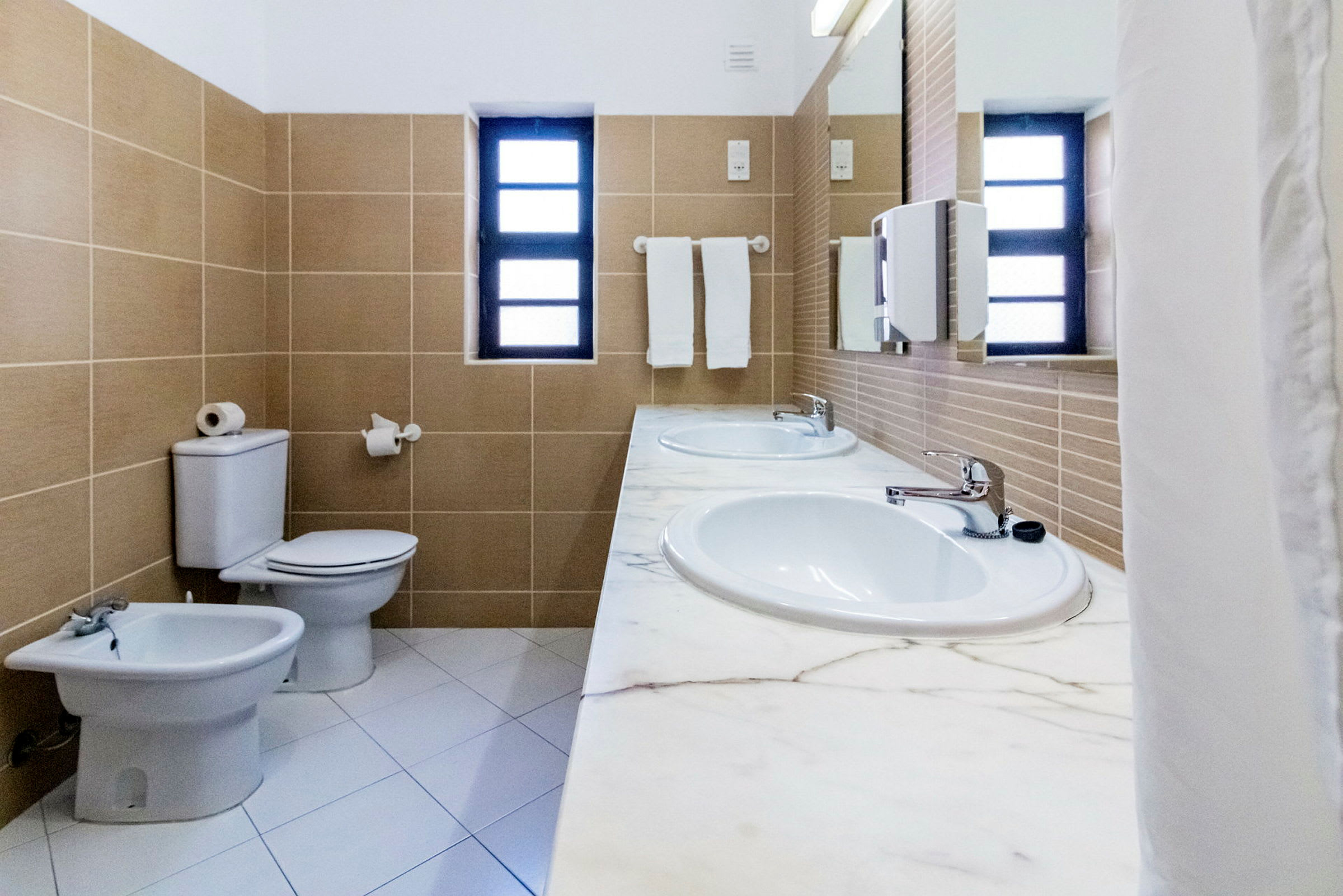 Badeværelse med to håndvaske, toilet, bidet og vindue. (AI-genereret tekst)