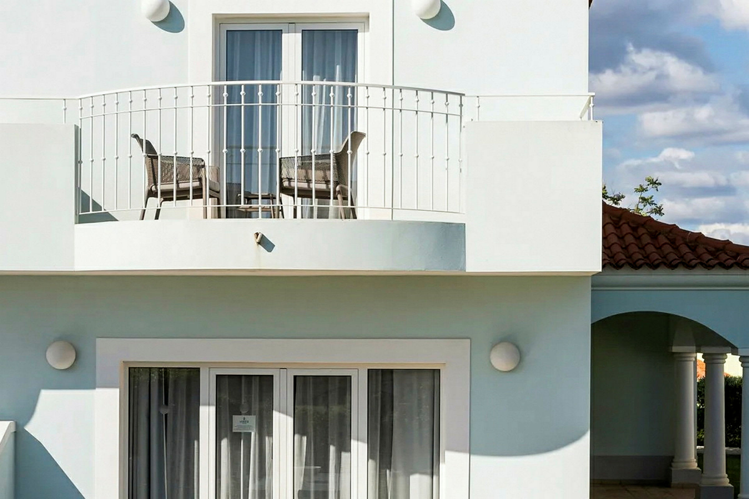 En bygning med en balkon med stole og bord samt vinduer og døre med hvide rammer. (AI-genereret tekst)