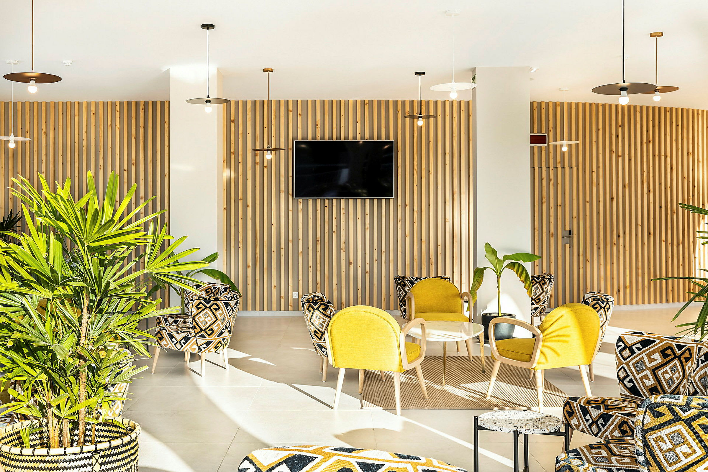 En lys og moderne lounge med gul og mønstret møblering samt grønne planter. (AI-genereret tekst)