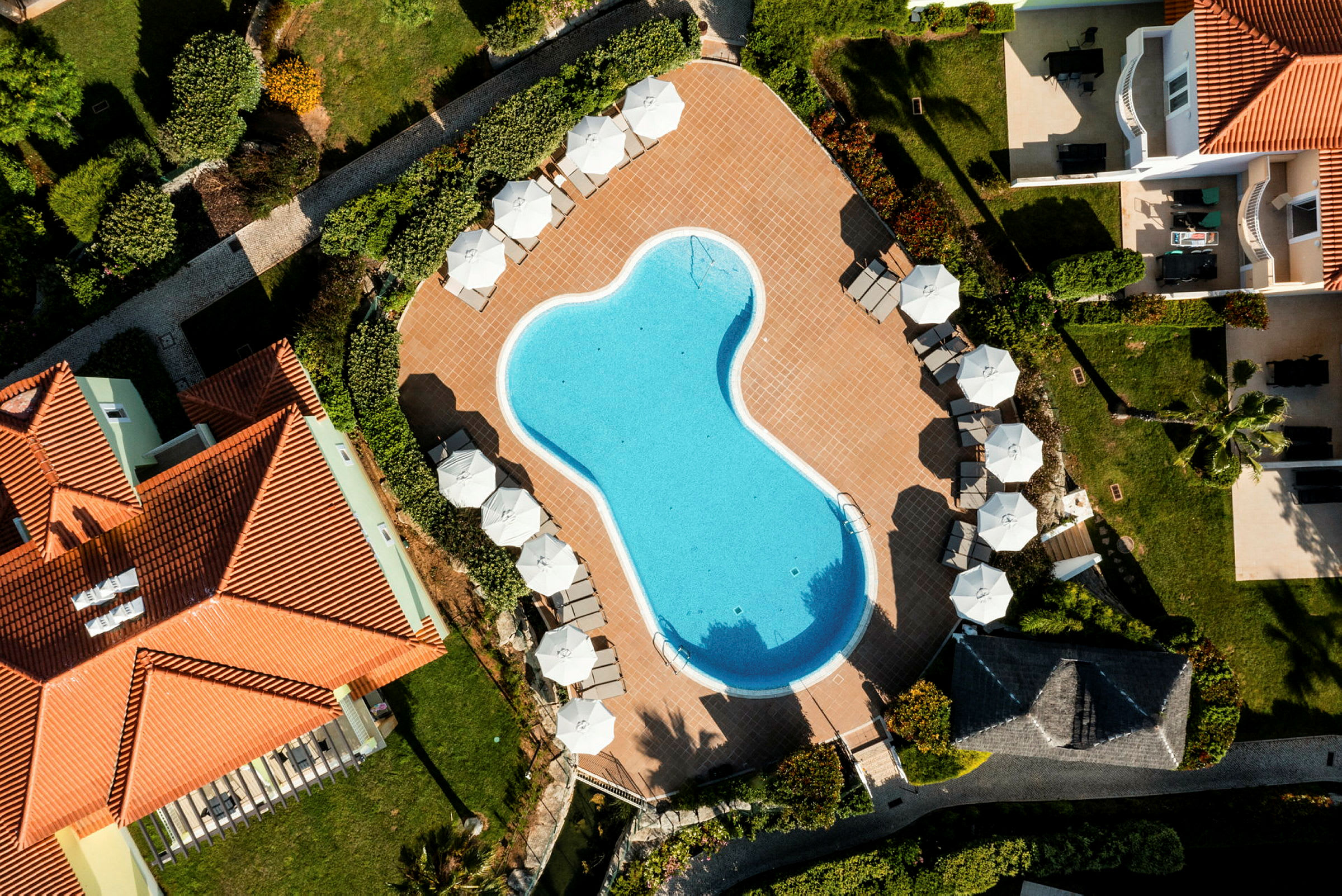 Luftfoto af en udendørs swimmingpool omgivet af parasoller og liggestole. (AI-genereret tekst)