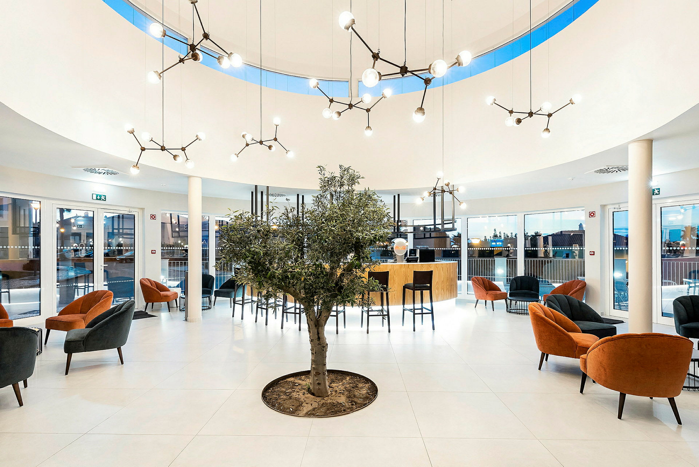 Moderne reception med siddegrupper, et oliventræ og elegante lysarmaturer. (AI-genereret tekst)