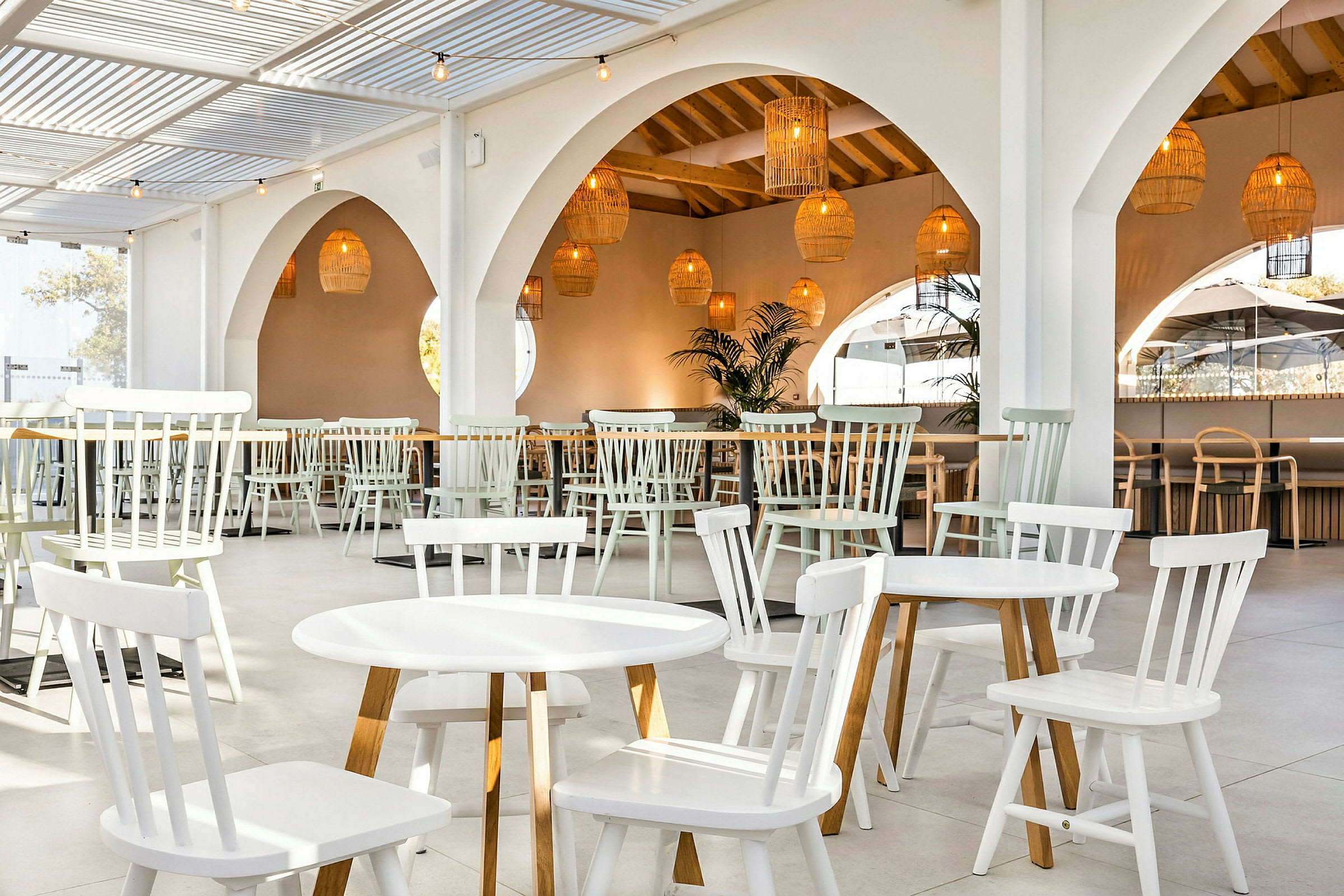 En lys restaurant med hvide træborde og stole samt hængende kurvelamper. (AI-genereret tekst)
