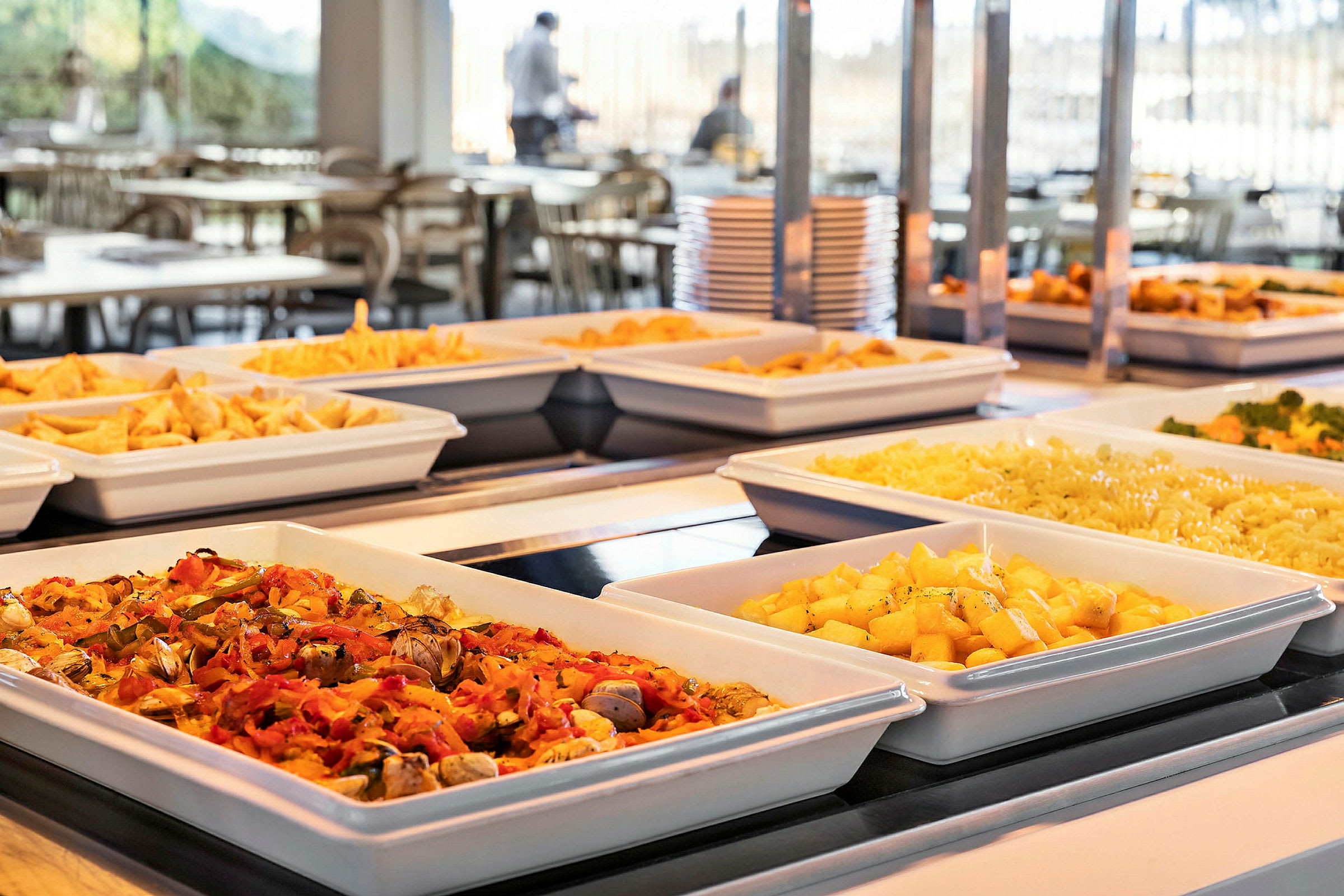 Billede af en buffet med forskellige retter, herunder kartofler, pasta og grøntsager, som er anrettet i hvide serveringsskåle. (AI-genereret tekst)