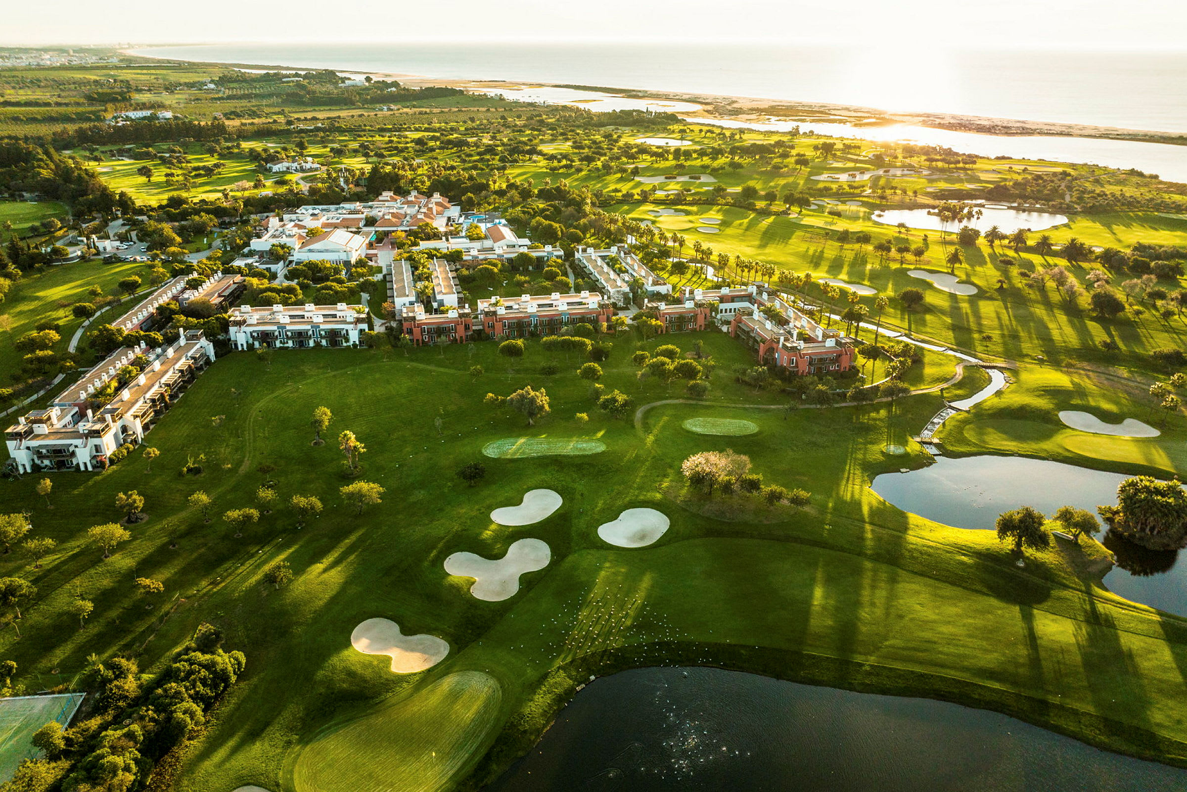 Luftbillede af grønne områder med bygninger og golfbaner ved havet. (AI-genereret tekst)