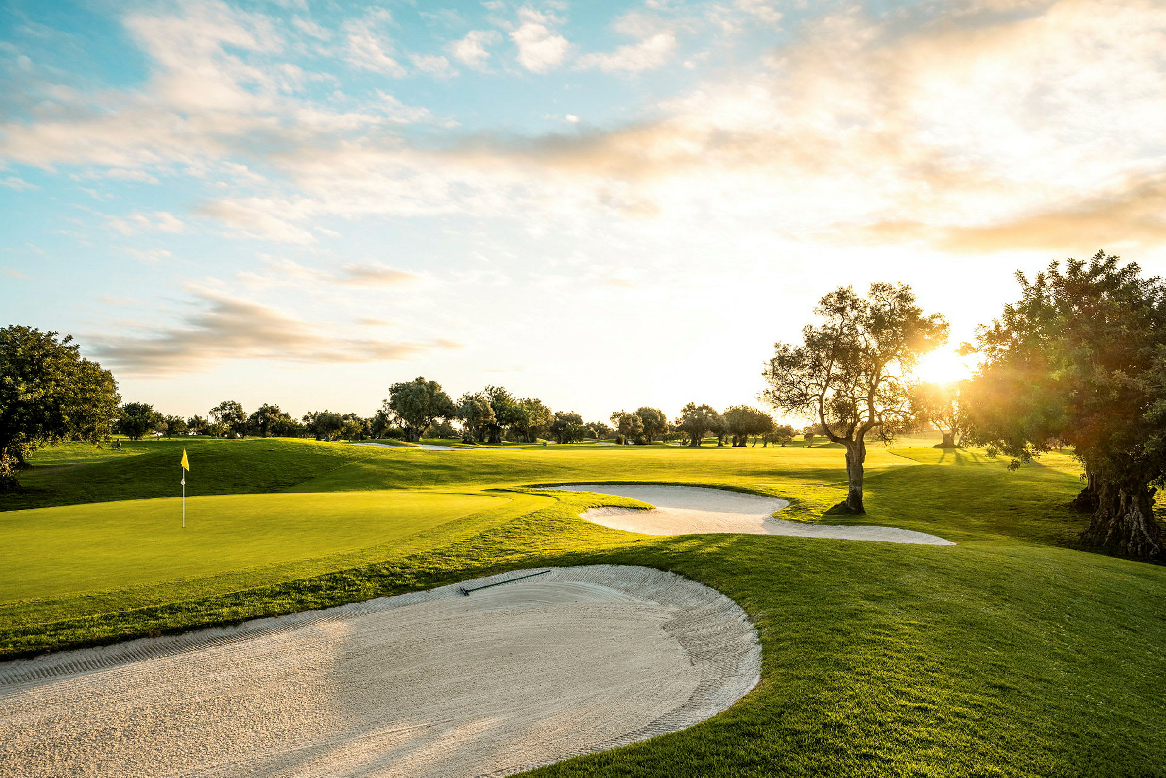 En golfbane med sandbunkers, solnedgang og træer. (AI-genereret tekst)