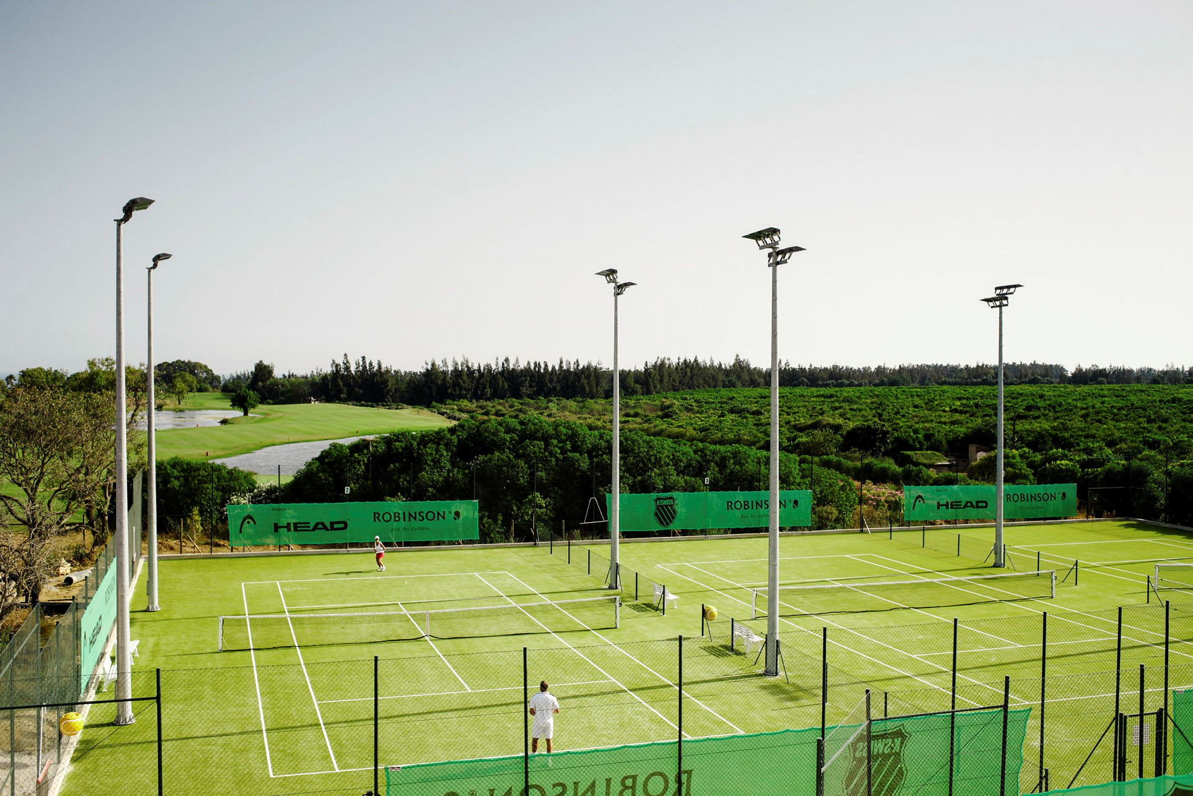 Tennisbaner med grønt underlag omgivet af natur. (AI-genereret tekst)