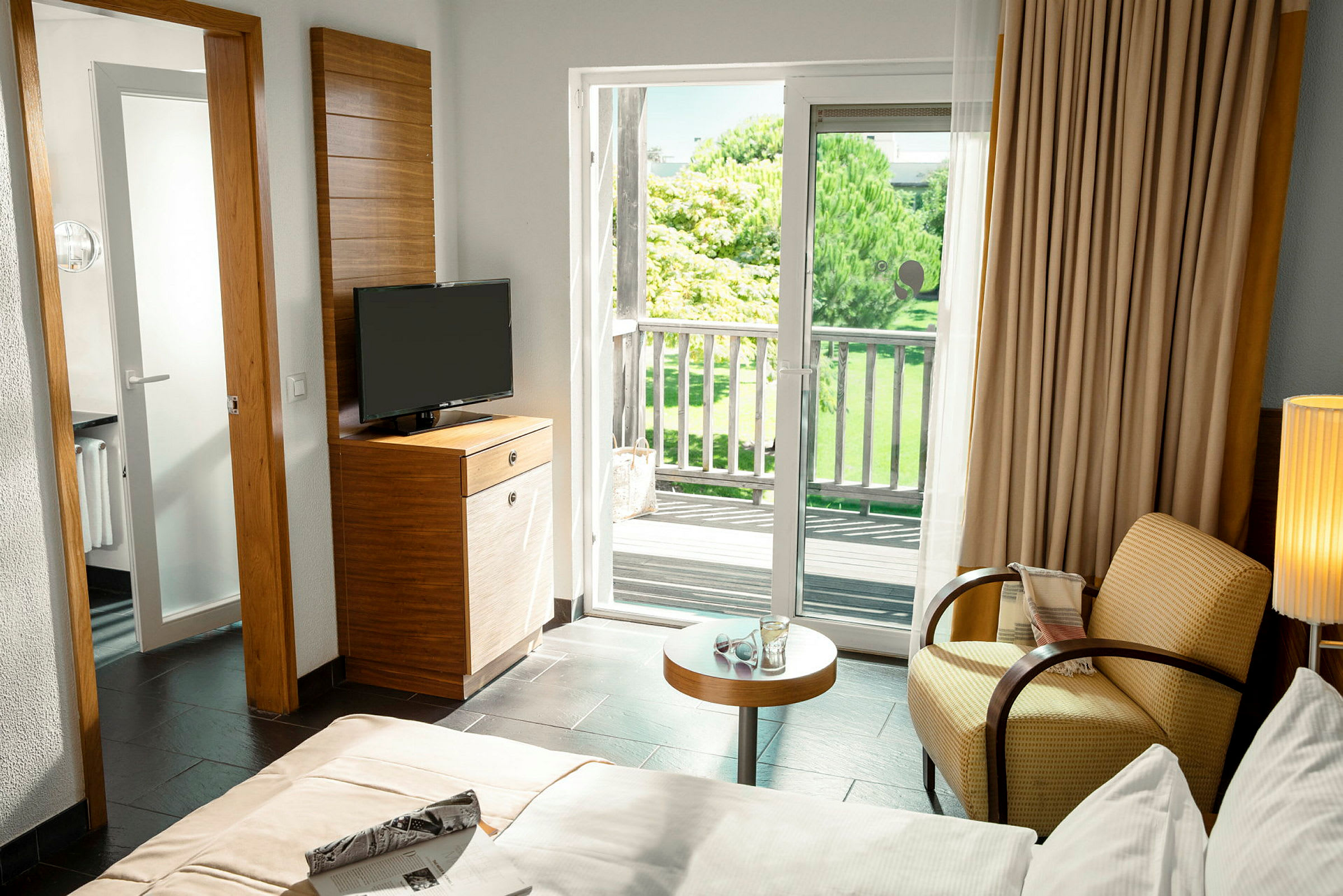 Et hotelværelse med en balkon og udsigt over grønne områder udenfor. (AI-genereret tekst)