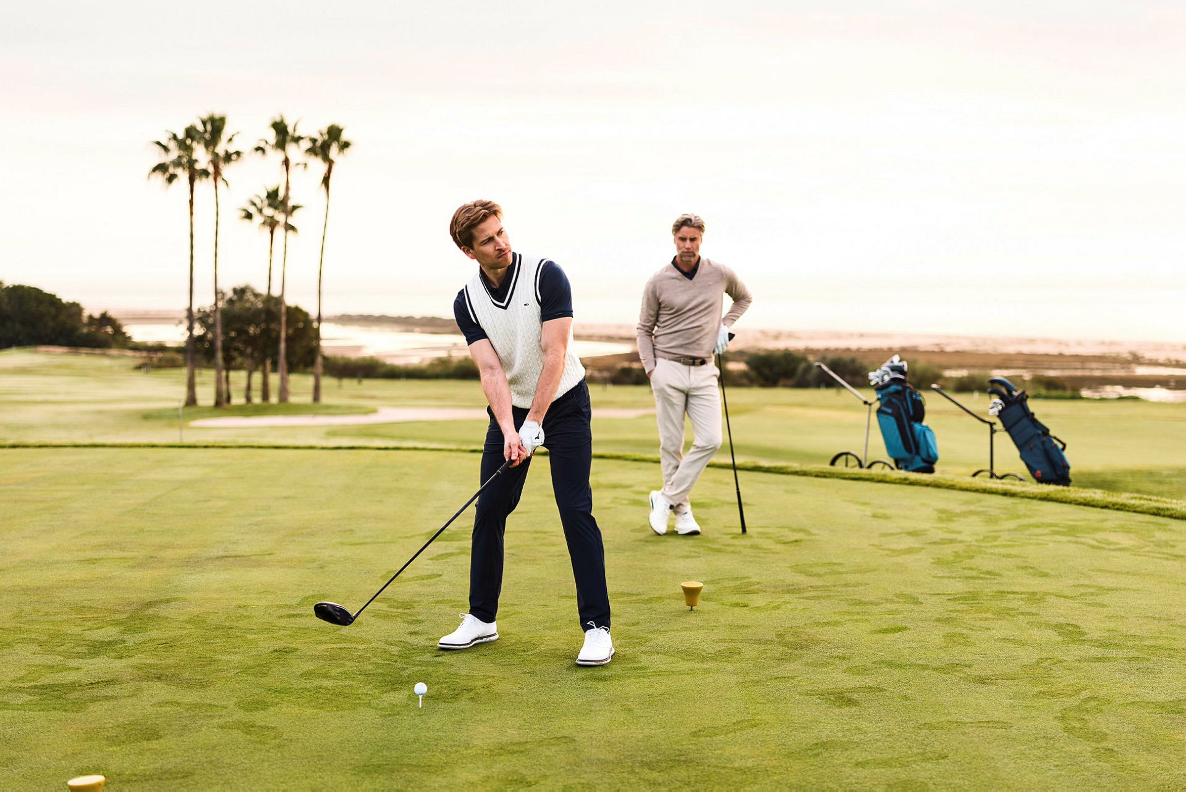 En person spiller golf, og en anden står ved siden af, med en grøn golfbane i baggrunden. (AI-genereret tekst)