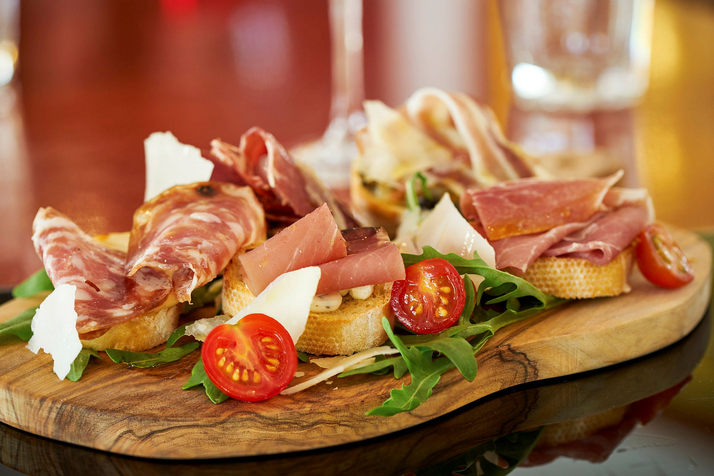 En træplade med antipasti inkluderende skiver af pålæg, cherrytomater, rucola og ost. (AI-genereret tekst)