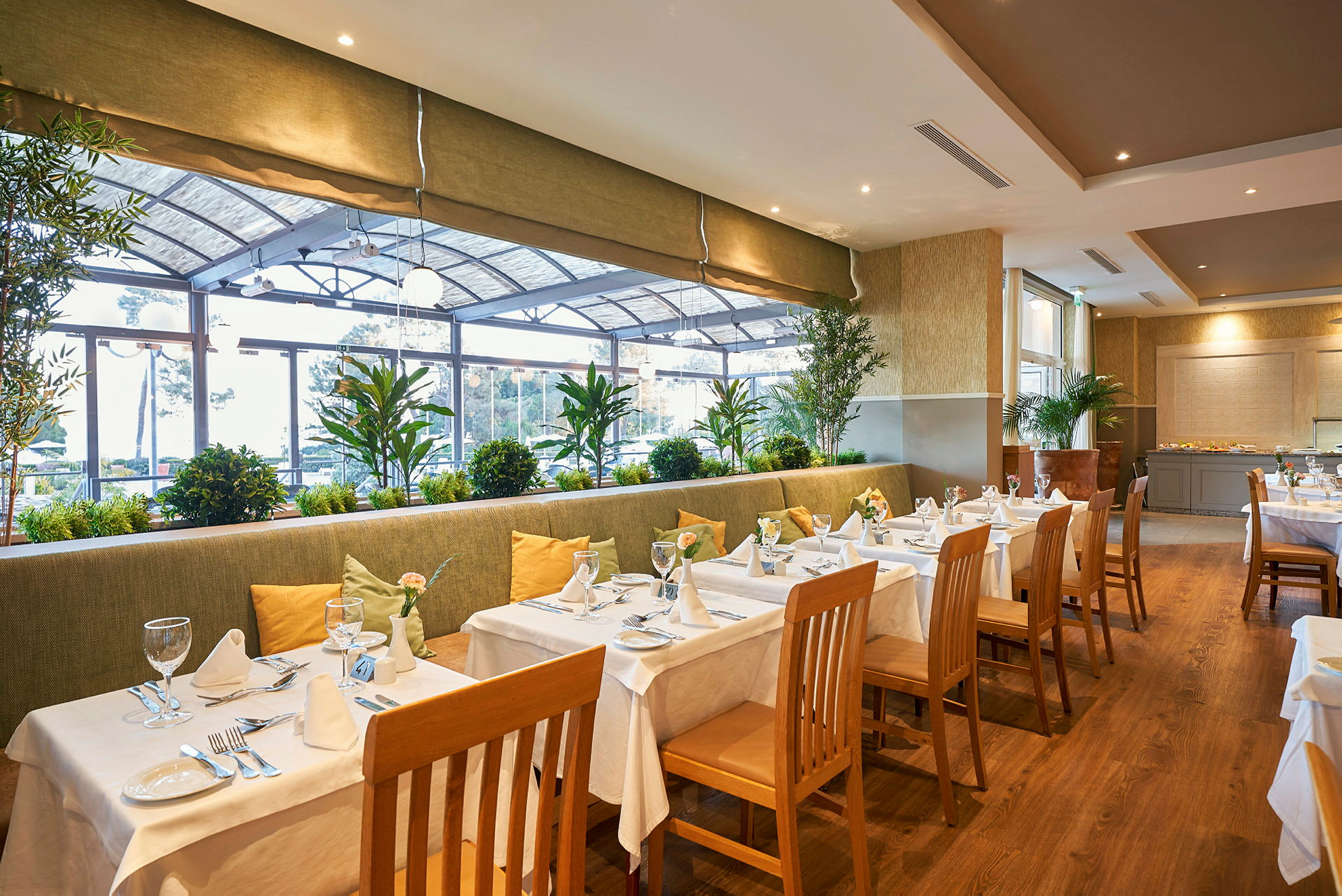 Restaurant med dækkede borde, stole og planter ved vinduet. (AI-genereret tekst)