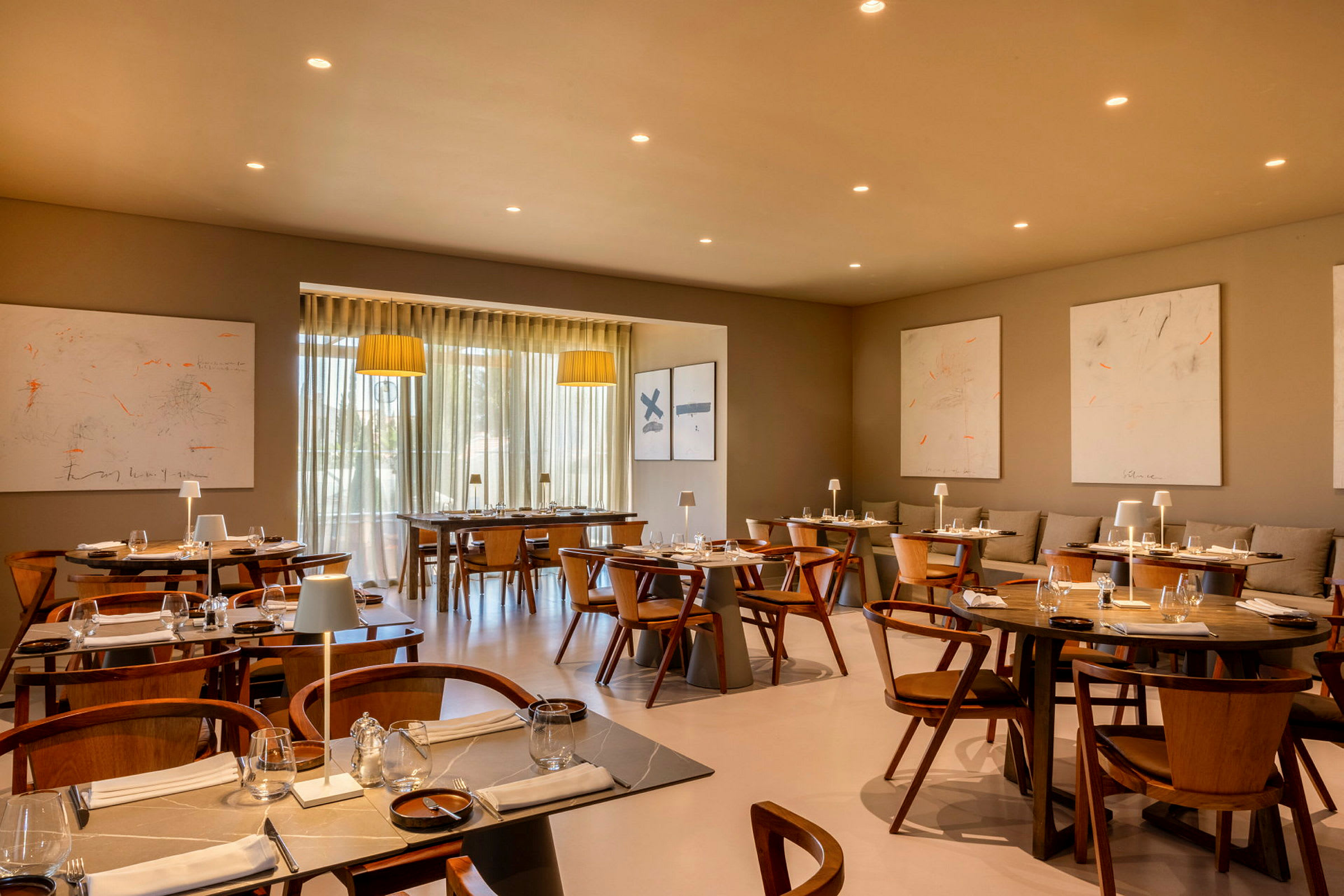 En moderne restaurant med træborde og stole, dekorativ belysning og kunstværker på væggen. (AI-genereret tekst)