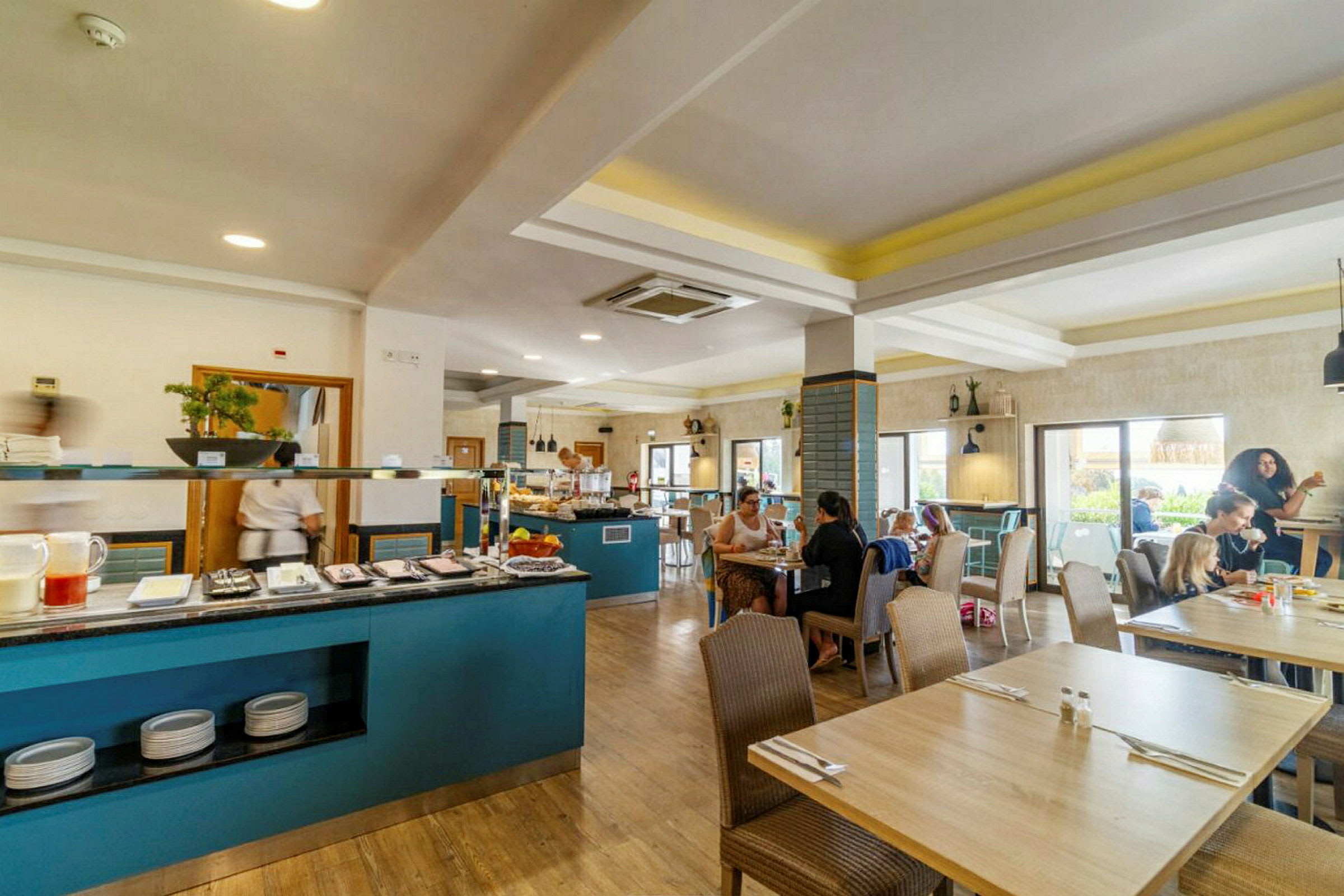 Restaurantmiljø med borde og mennesker, samt en buffetskank med mad og drikke. (AI-genereret tekst)