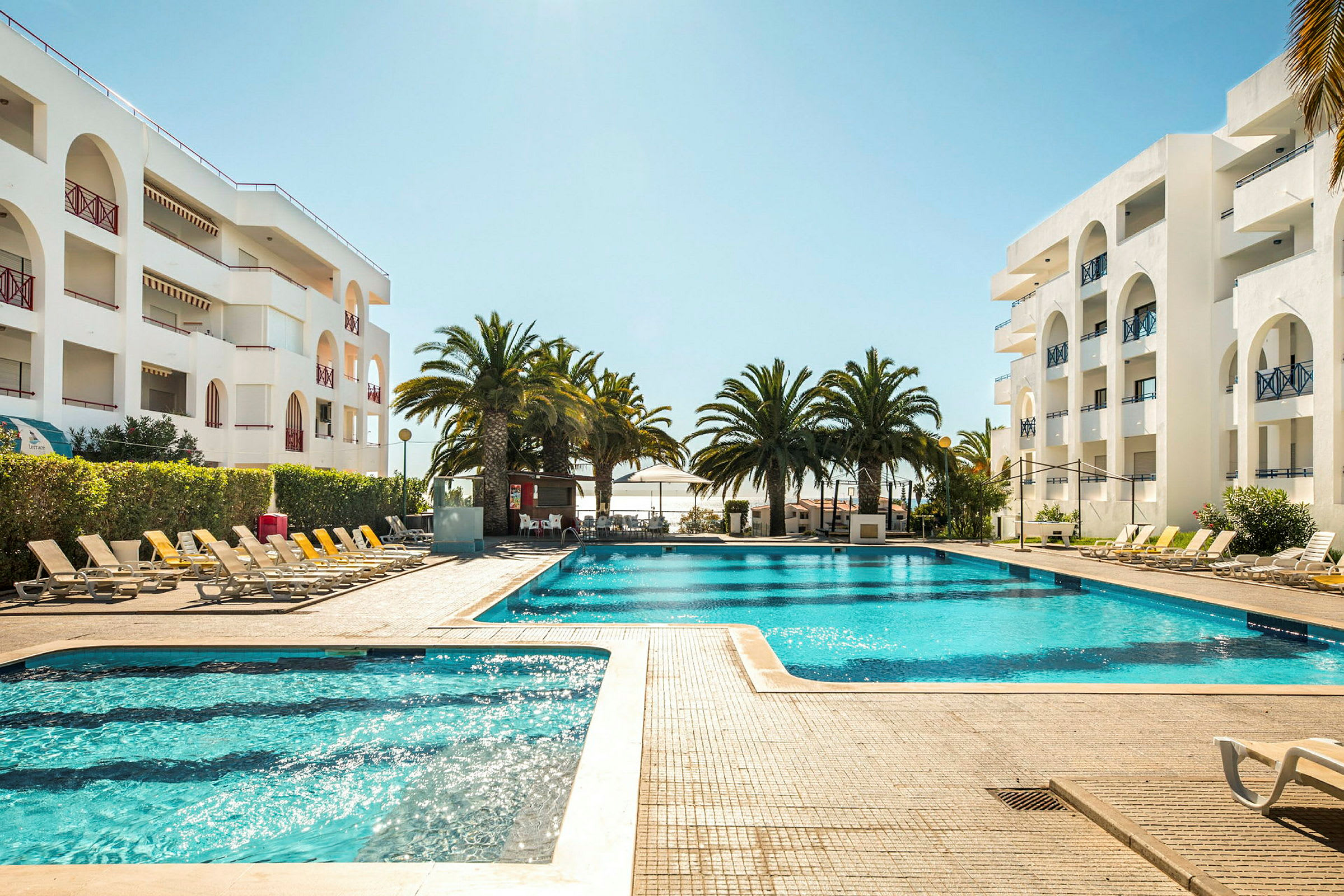 Udendørs pool omgivet af liggestole og palmer ved et hotel. (AI-genereret tekst)