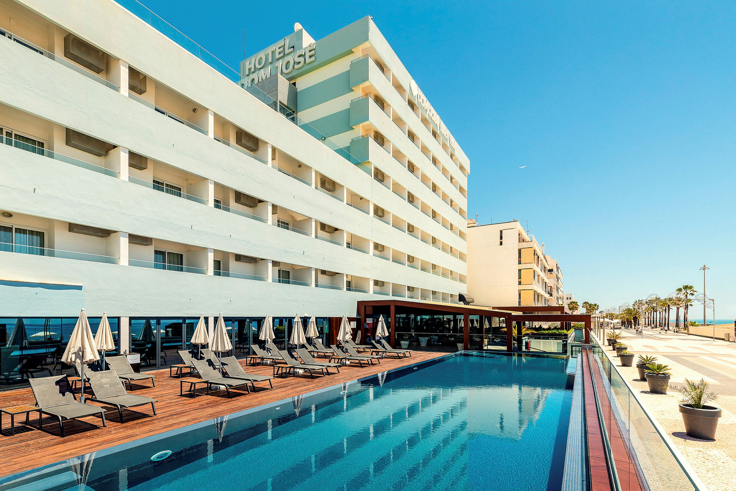 Hotelbygning med pool og liggestole. (AI-genereret tekst)