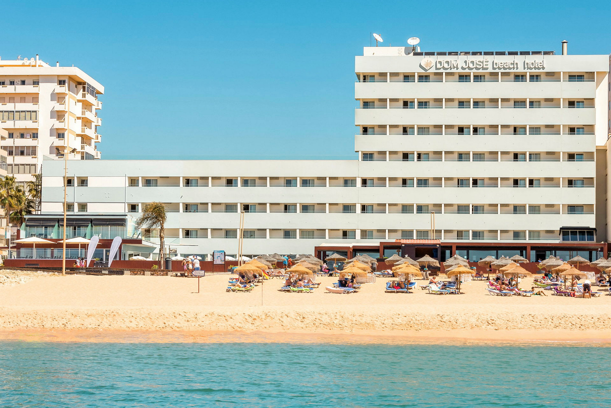 Hotel ved stranden med parasoller og liggestole. (AI-genereret tekst)