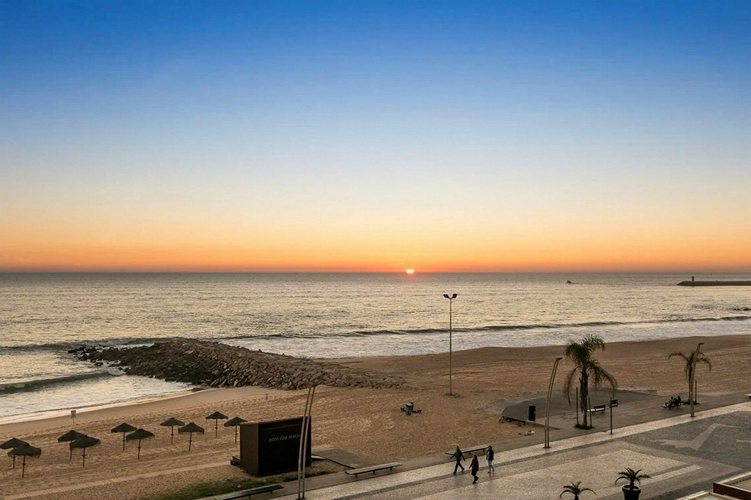 Solnedgang over en strand med parasoller og gangsti. (AI-genereret tekst)