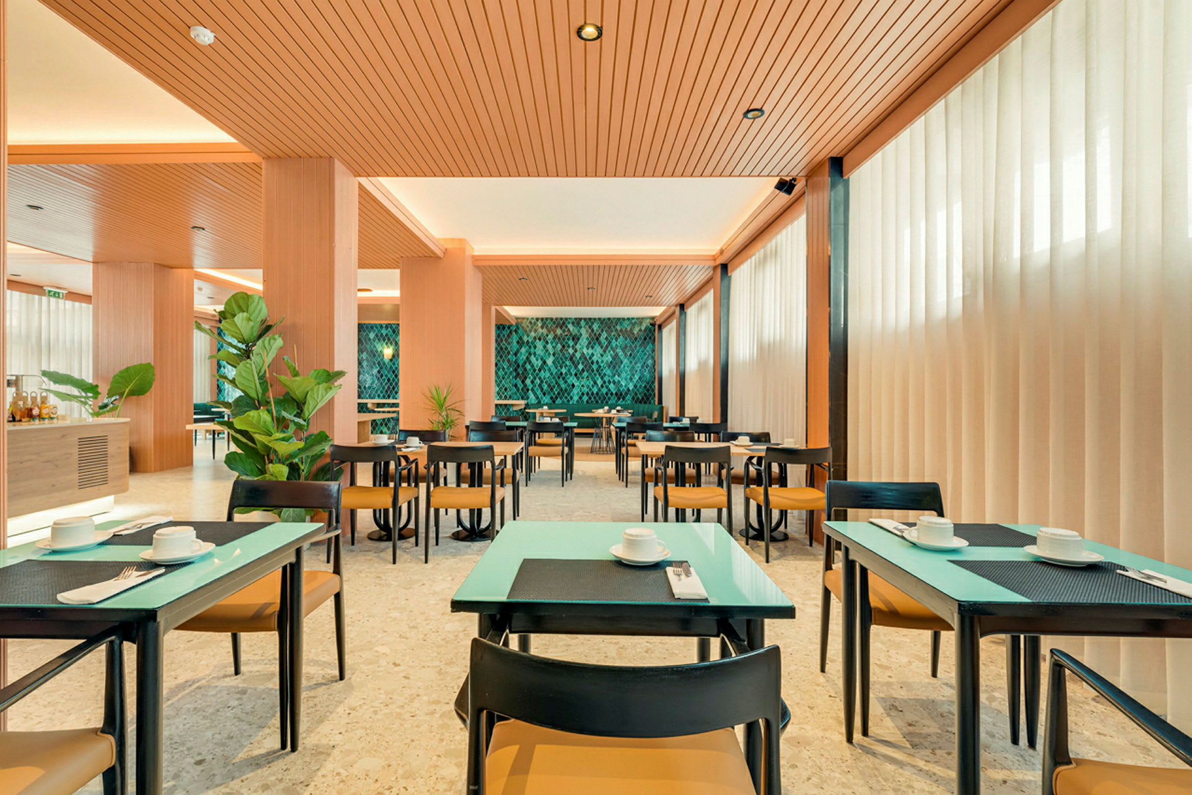 En lys og moderne restaurant med dækkede borde, grønne planter og en dekorativ væg. (AI-genereret tekst)
