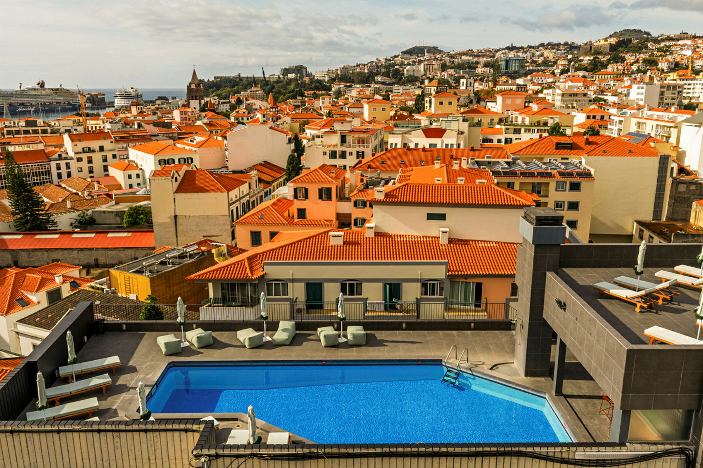 Udsigt over en by med huse med røde tage og en udendørs pool i forgrunden. (AI-genereret tekst)