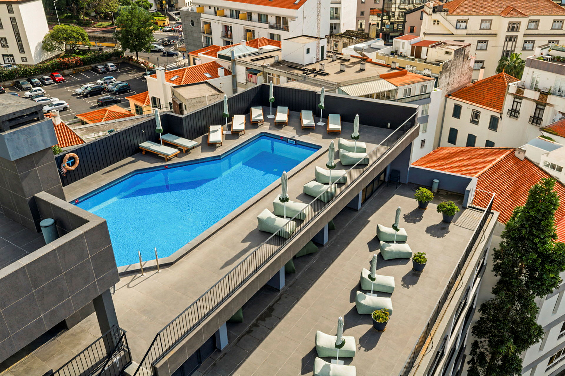 En tagterrasse med en pool, liggestole og parasoller. Omkringliggende bygninger ses. (AI-genereret tekst)