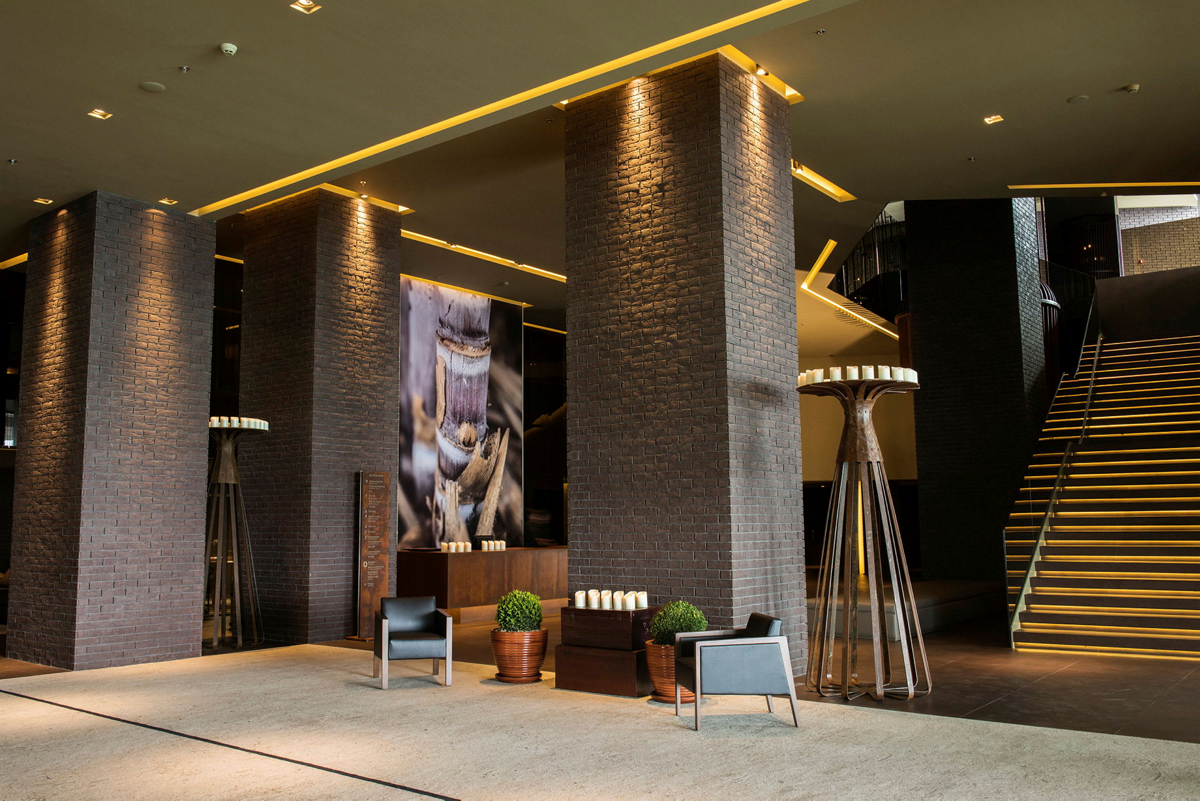 En moderne hotellobby med mørke murstenssøjler, dekorerede vægge og en oplyst trappe. (AI-genereret tekst)