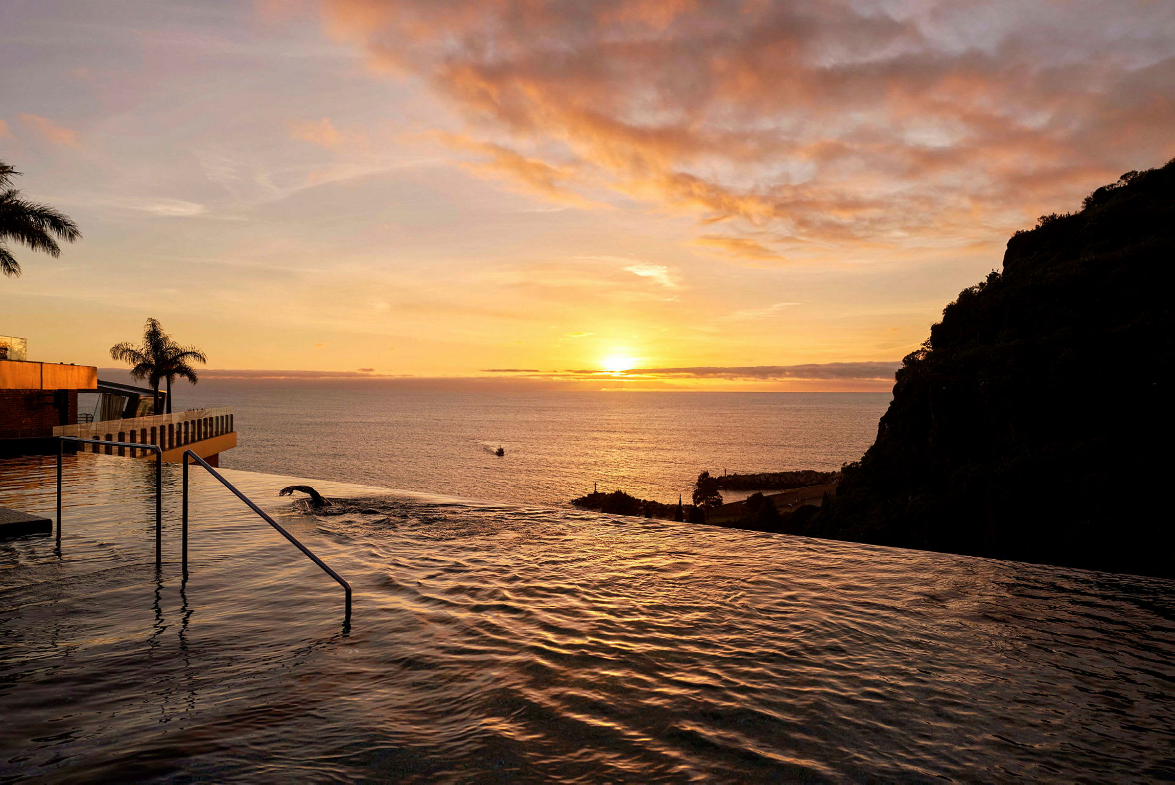 Udsigt over en infinitivpool med havet og solnedgangen i baggrunden. (AI-genereret tekst)