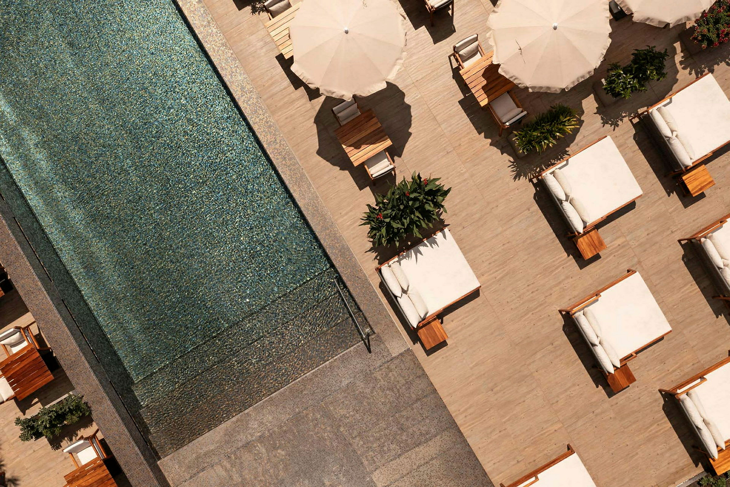 Udsigt ovenfra af en pool ved siden af en terrasse med solsenge og parasoller. (AI-genereret tekst)